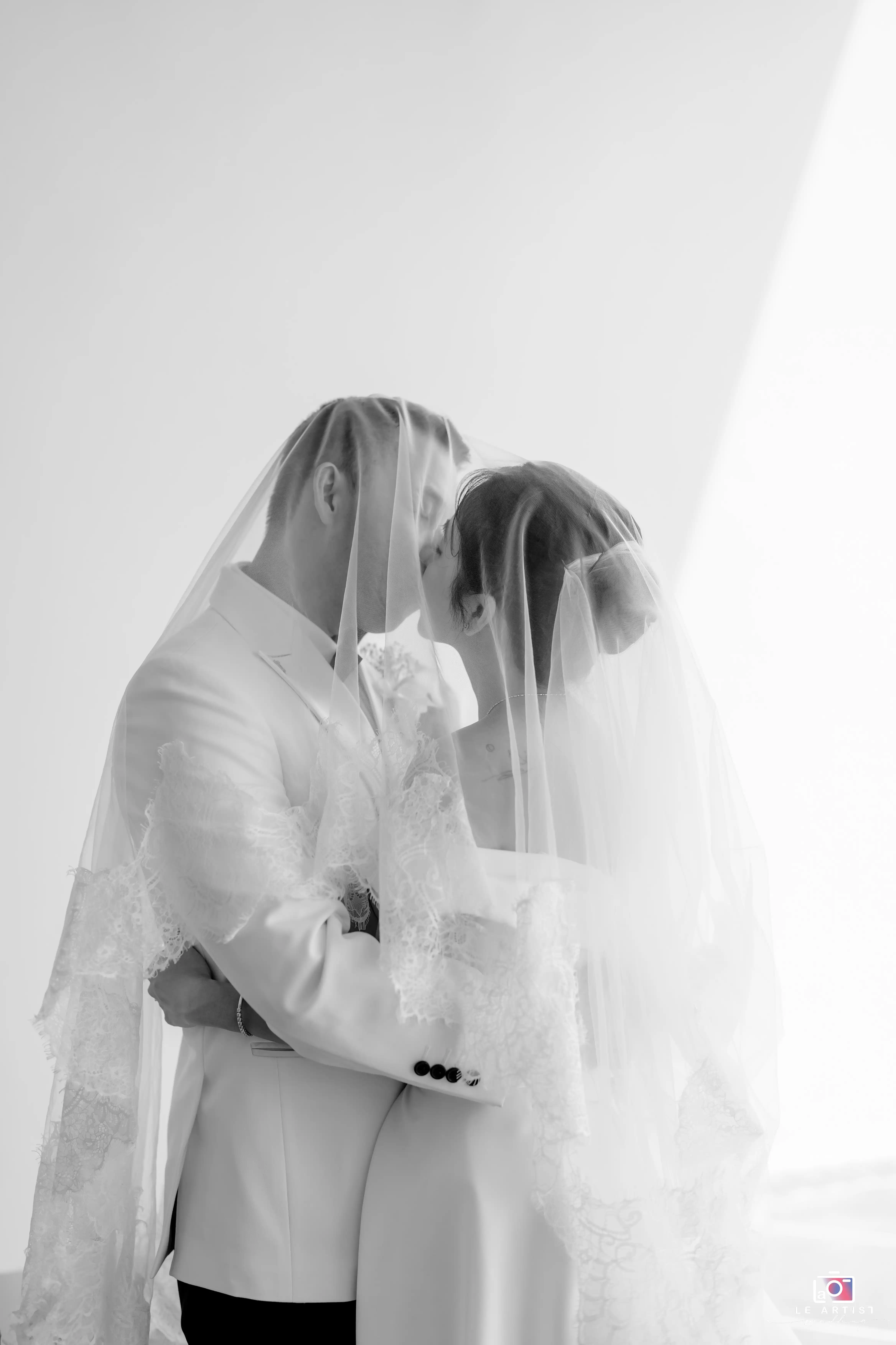 A romantic black and white portrait of the bride and groom sharing a kiss under the veil. Le Artist Wedding