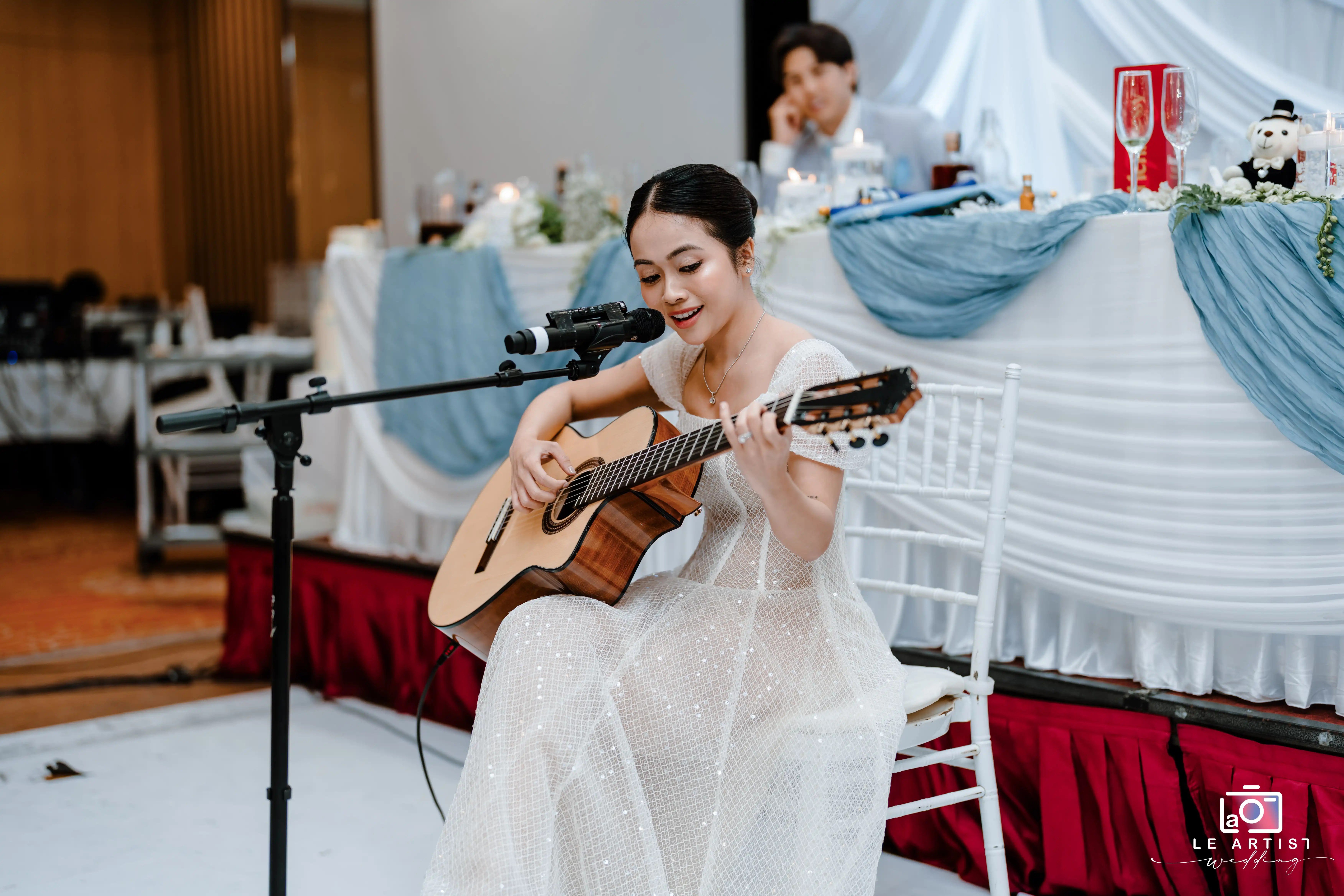 A bridesmaid elegantly performs a heartfelt song on the guitar during the wedding celebration, adding a personal and touching touch to the event. Le Artist Wedding