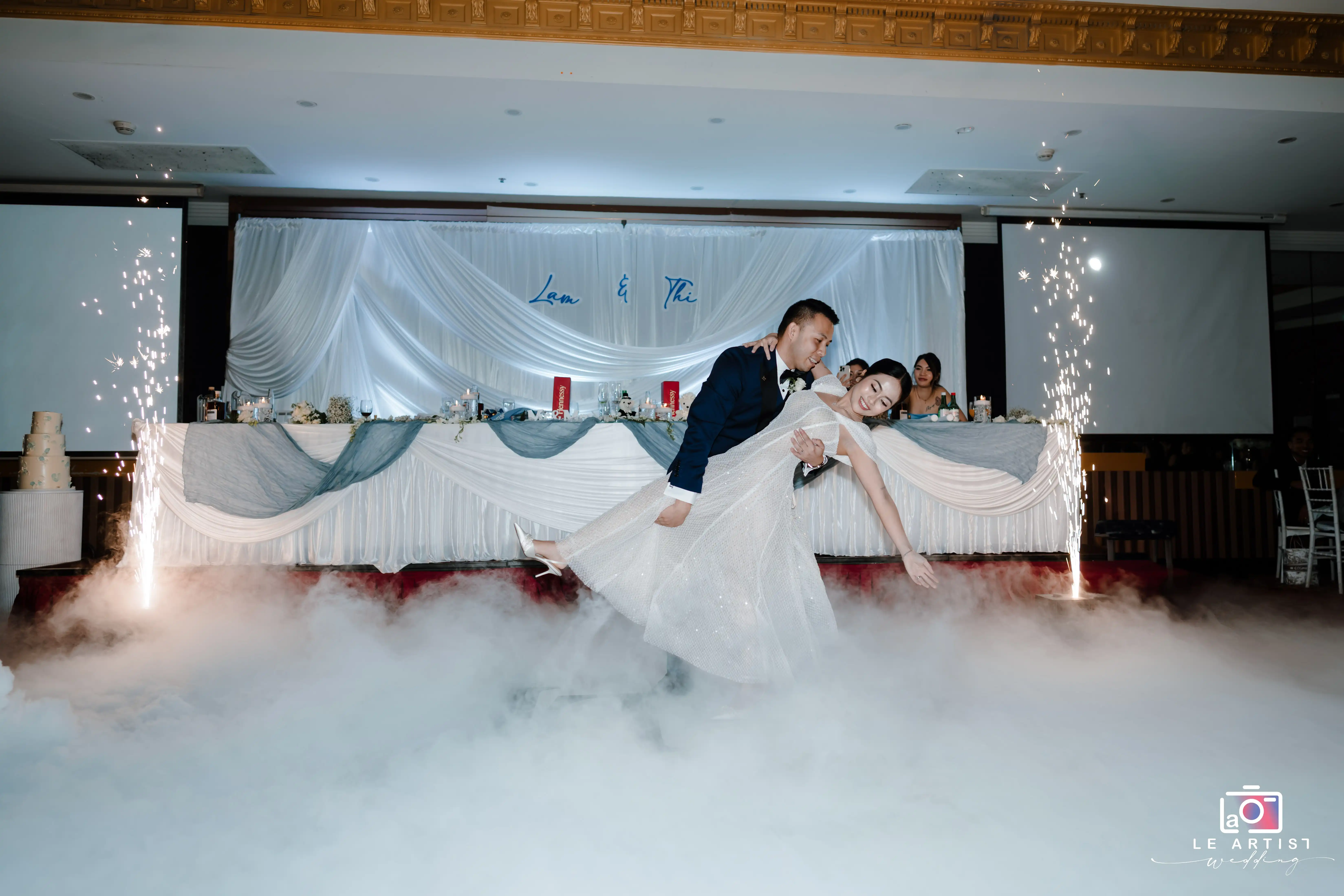 The couple shares a joyful dance with a dramatic dip, surrounded by enchanting mist and sparkling lights on the stage. Le Artist Wedding