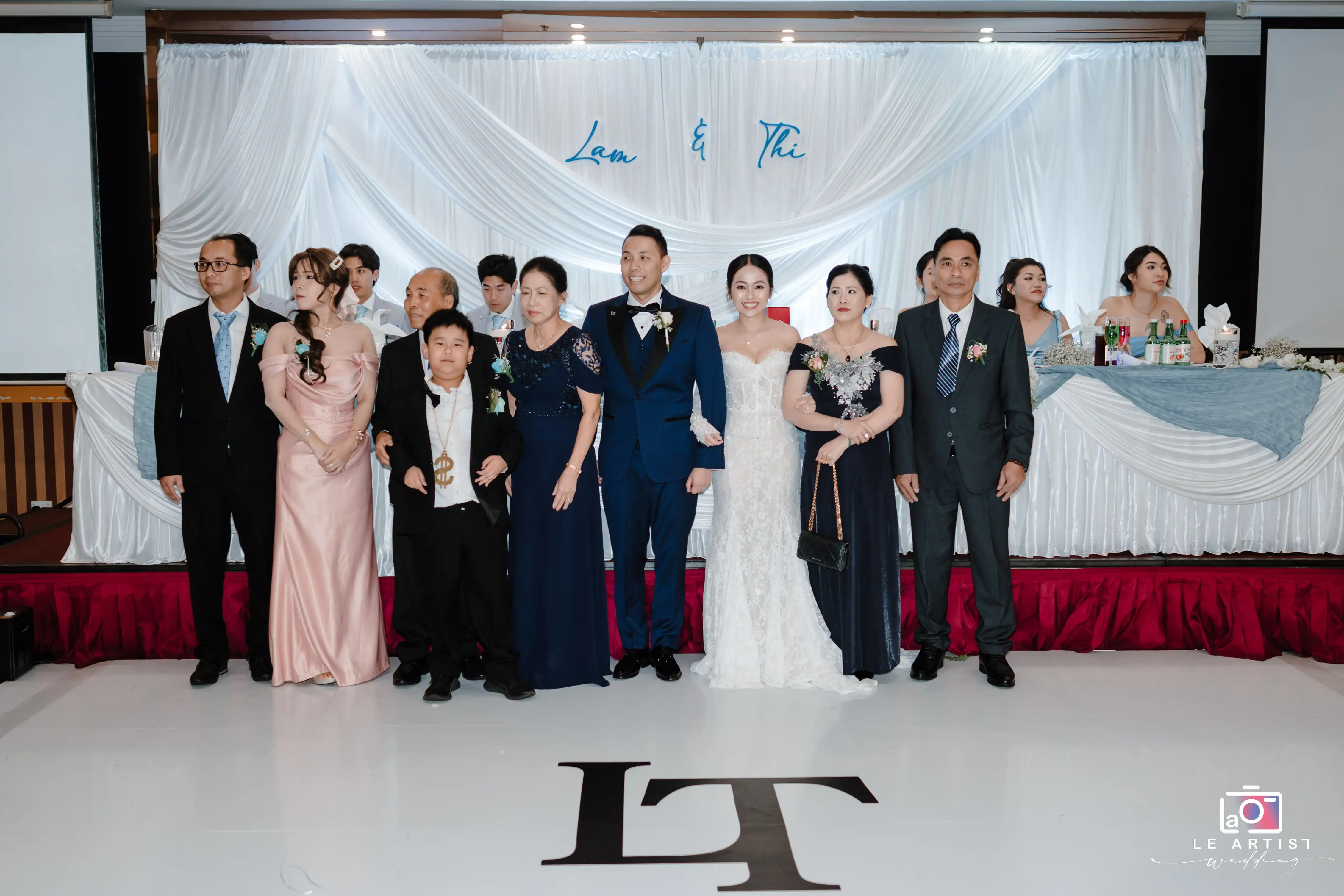 A joyful family gathers around the newlyweds for a memorable photo, capturing the essence of their special day. Le Artist Wedding