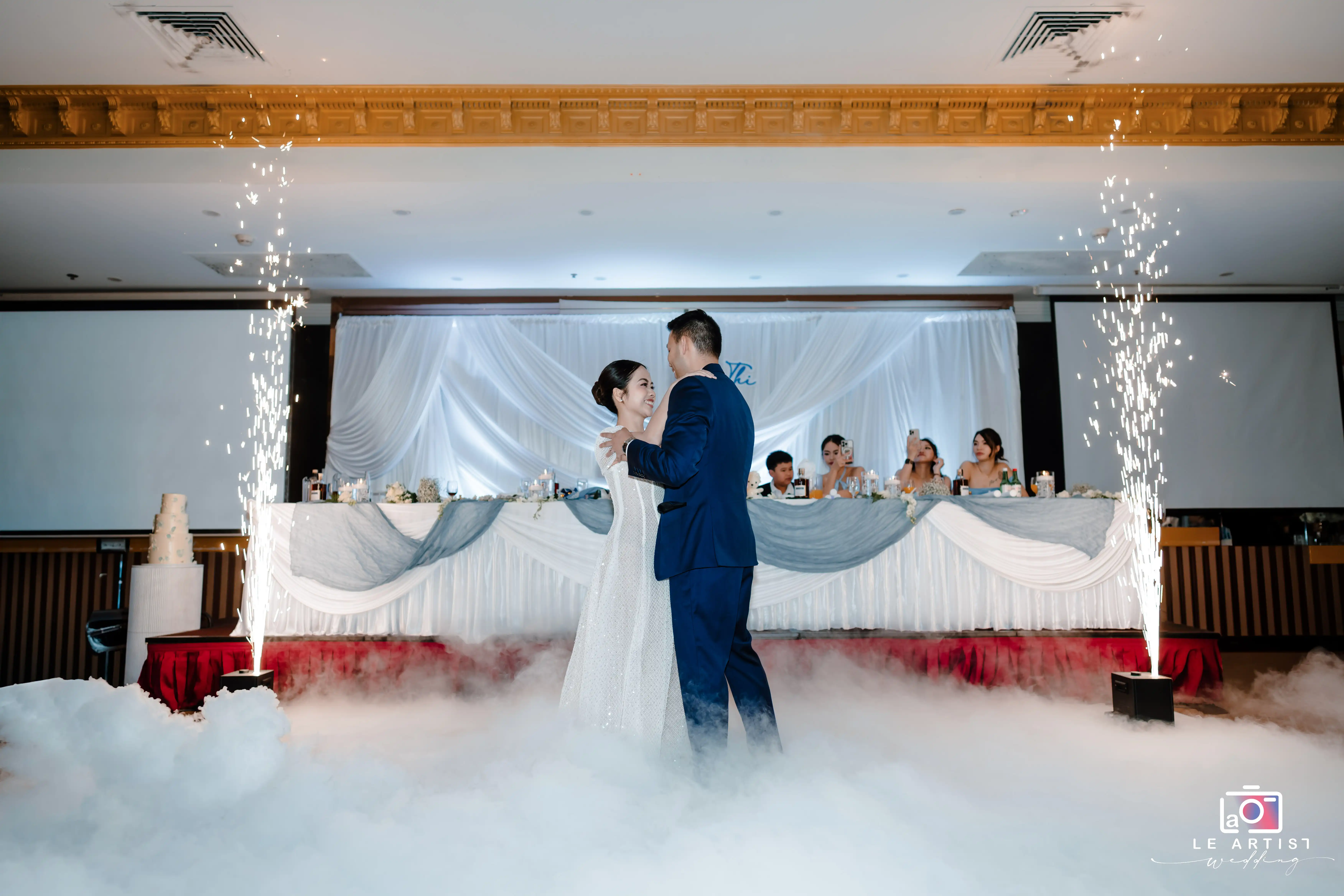 The couple shares a romantic first dance surrounded by mist and sparklers, creating an enchanting atmosphere at their wedding reception. Le Artist Wedding