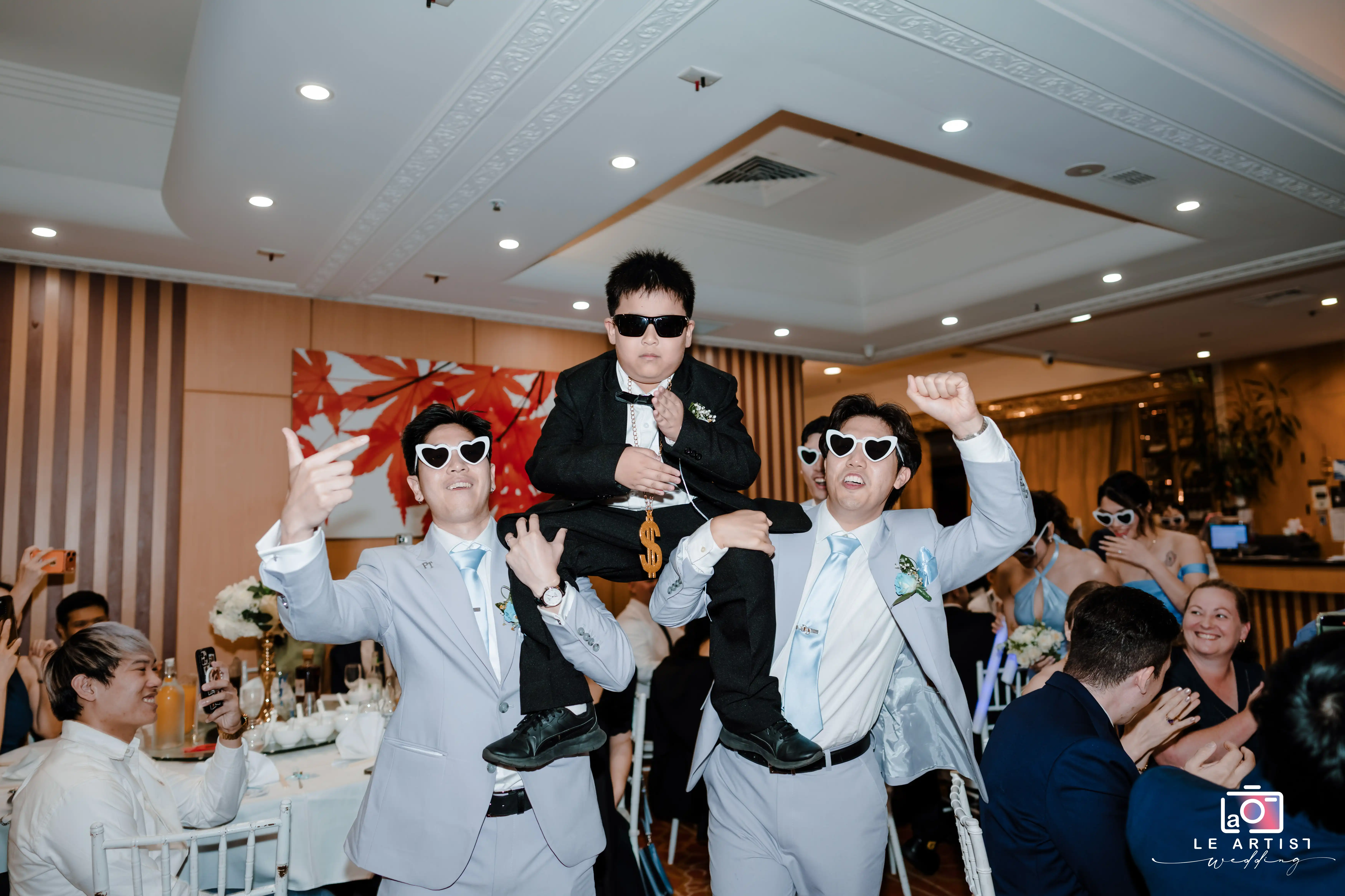 Groomsmen celebrate with a young guest in style, wearing matching heart-shaped sunglasses at the wedding reception. Le Artist Wedding