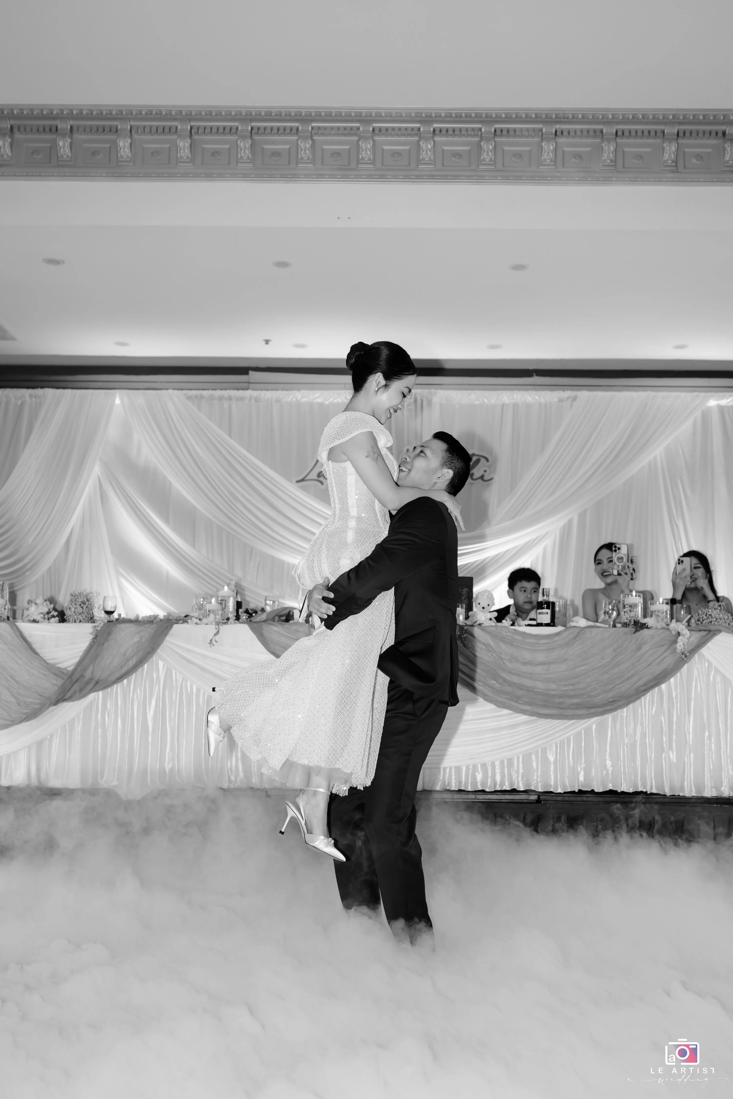 A joyful lift on the dance floor amidst a dreamy cloud of mist, capturing a magical wedding moment. Le Artist Wedding