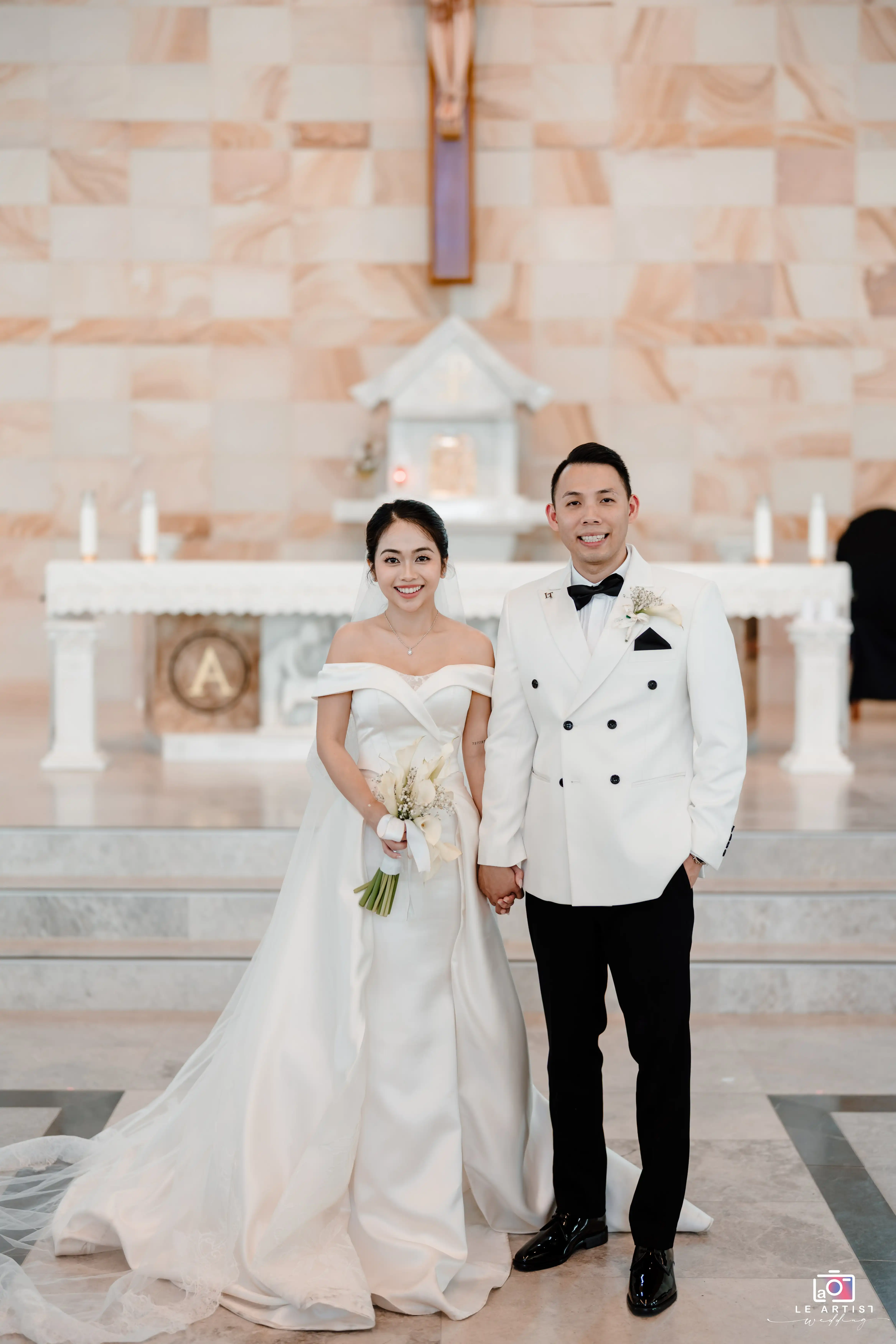 The newlyweds stand together in a beautiful church setting, showcasing their elegant attire and joyful smiles as they celebrate their special day. Le Artist Wedding