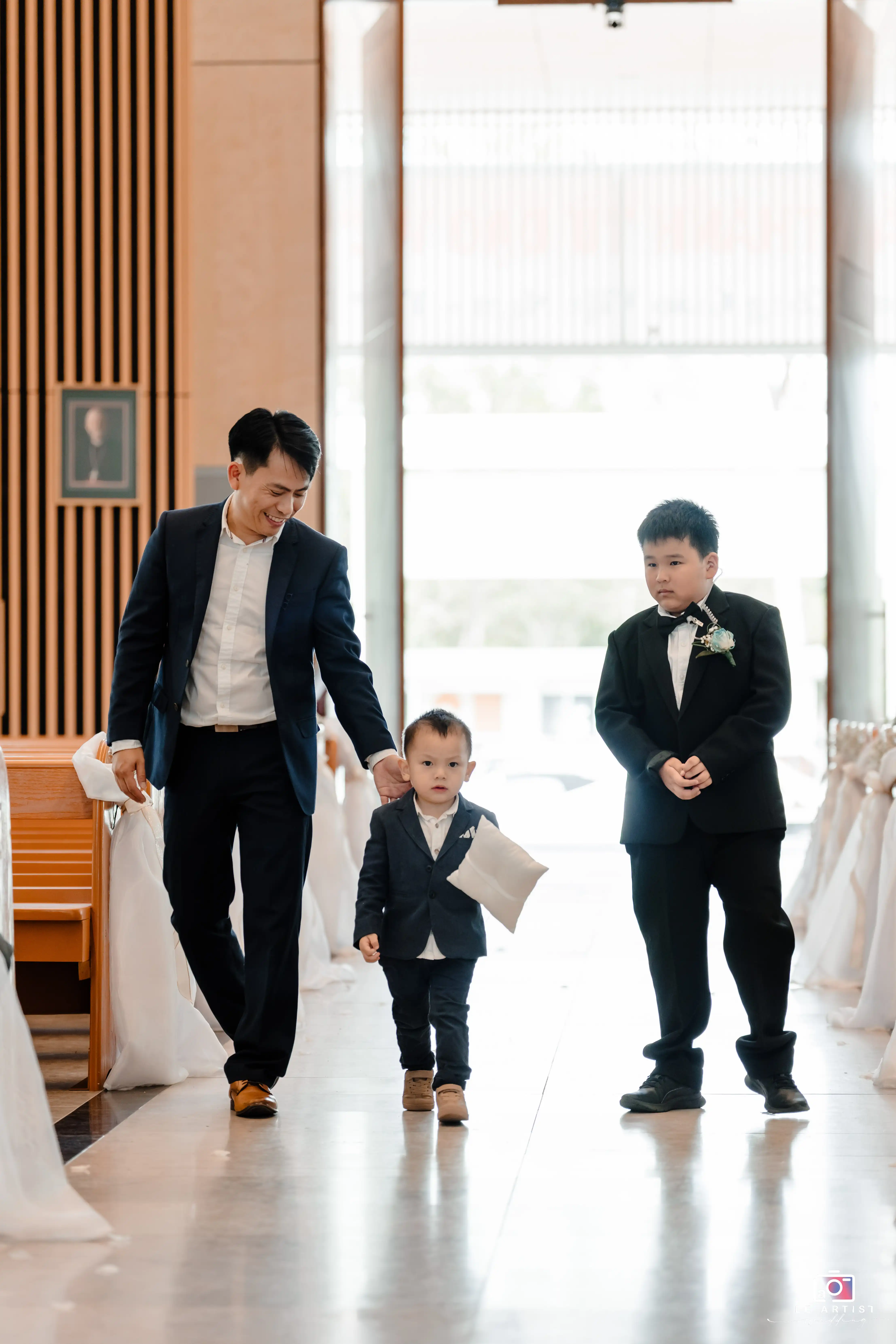 A sweet moment as the little ring bearer, assisted by an adult, walks down the aisle with a young usher by his side, signifying a charming start to the wedding ceremony. Le Artist Wedding