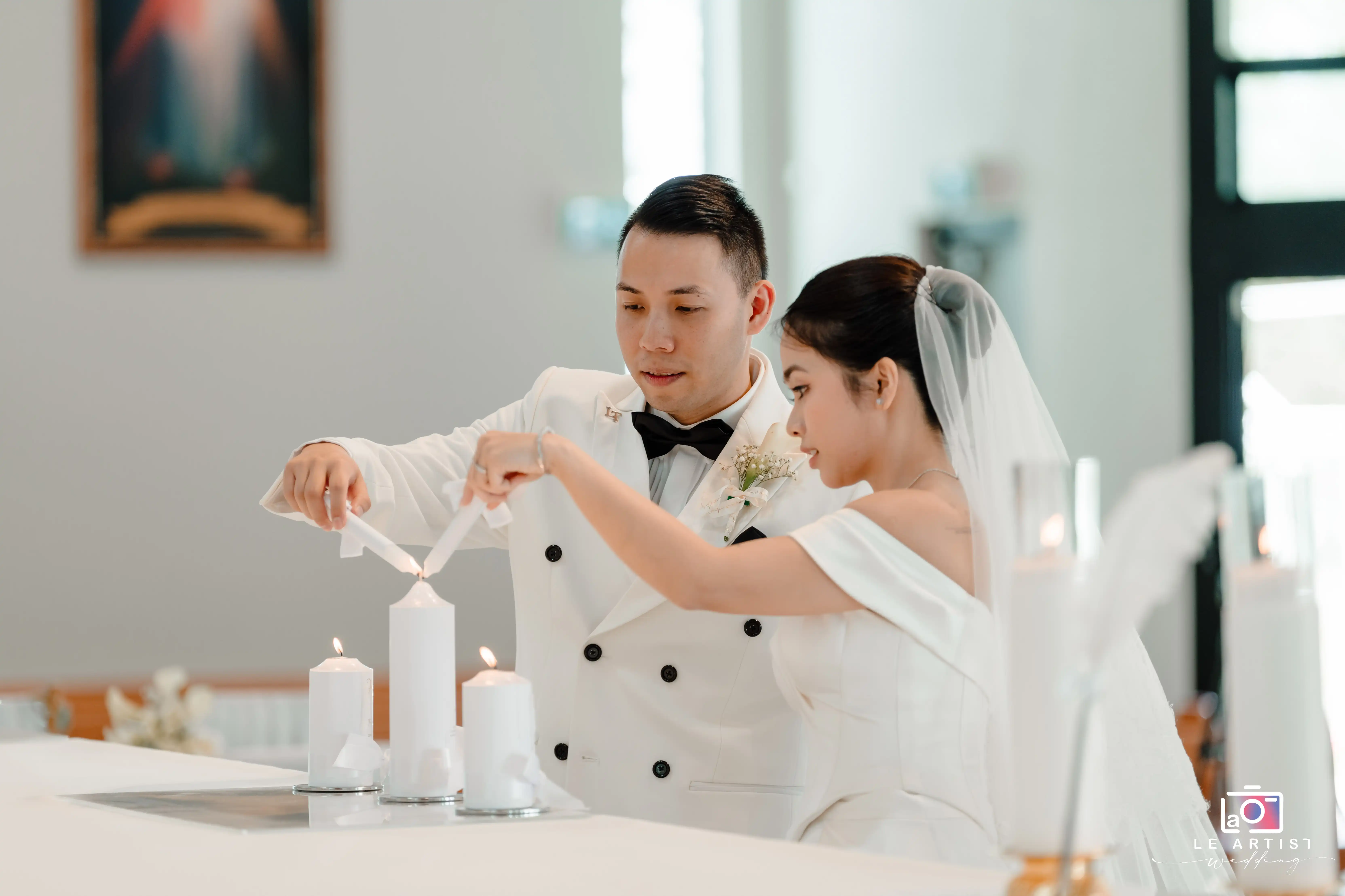 A couple performs the elegant unity candle ceremony, symbolizing their union as they light a candle together during their wedding. Le Artist Wedding