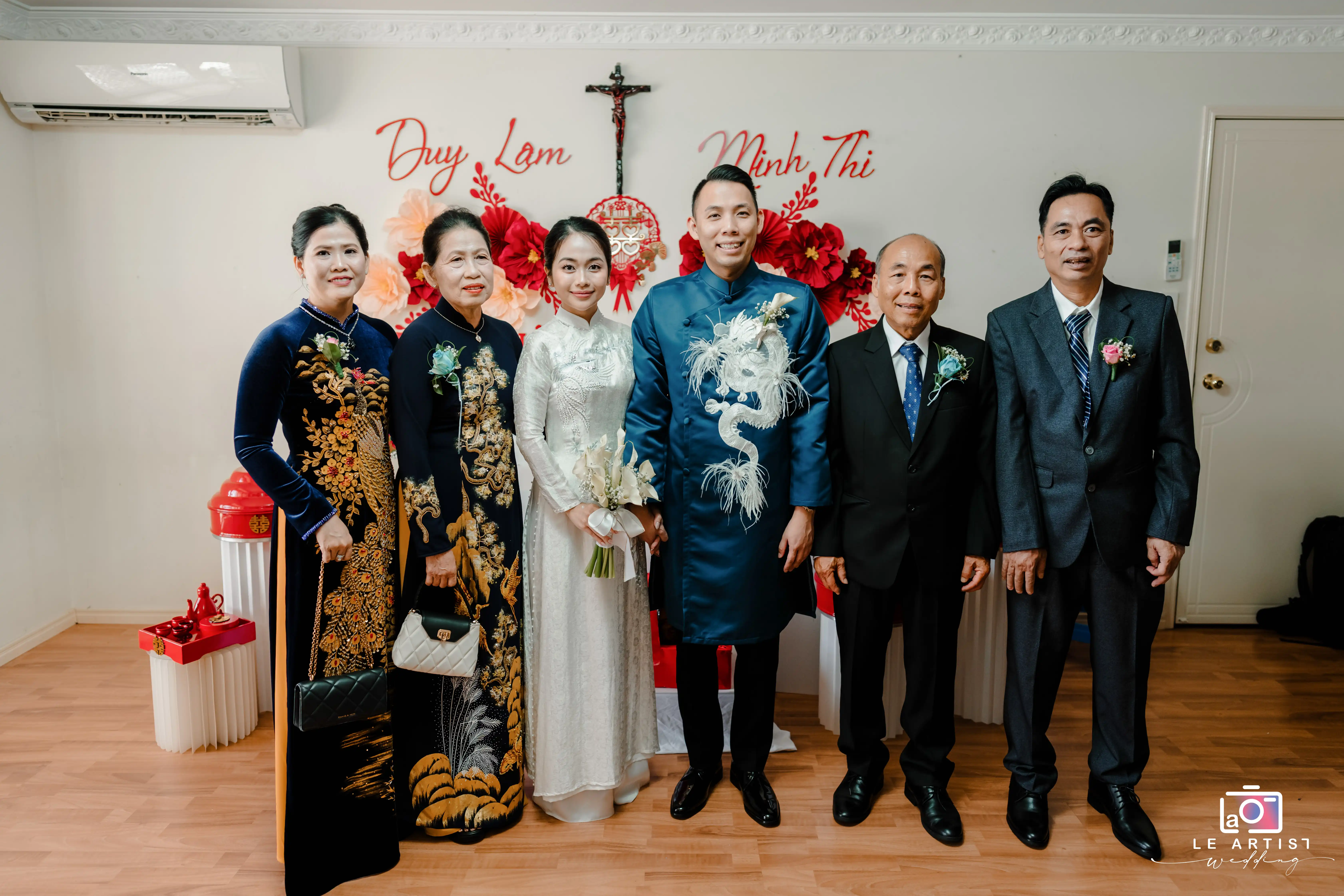 A joyous family portrait with the bride and groom wearing traditional attire, surrounded by elegantly dressed family members. Le Artist Wedding