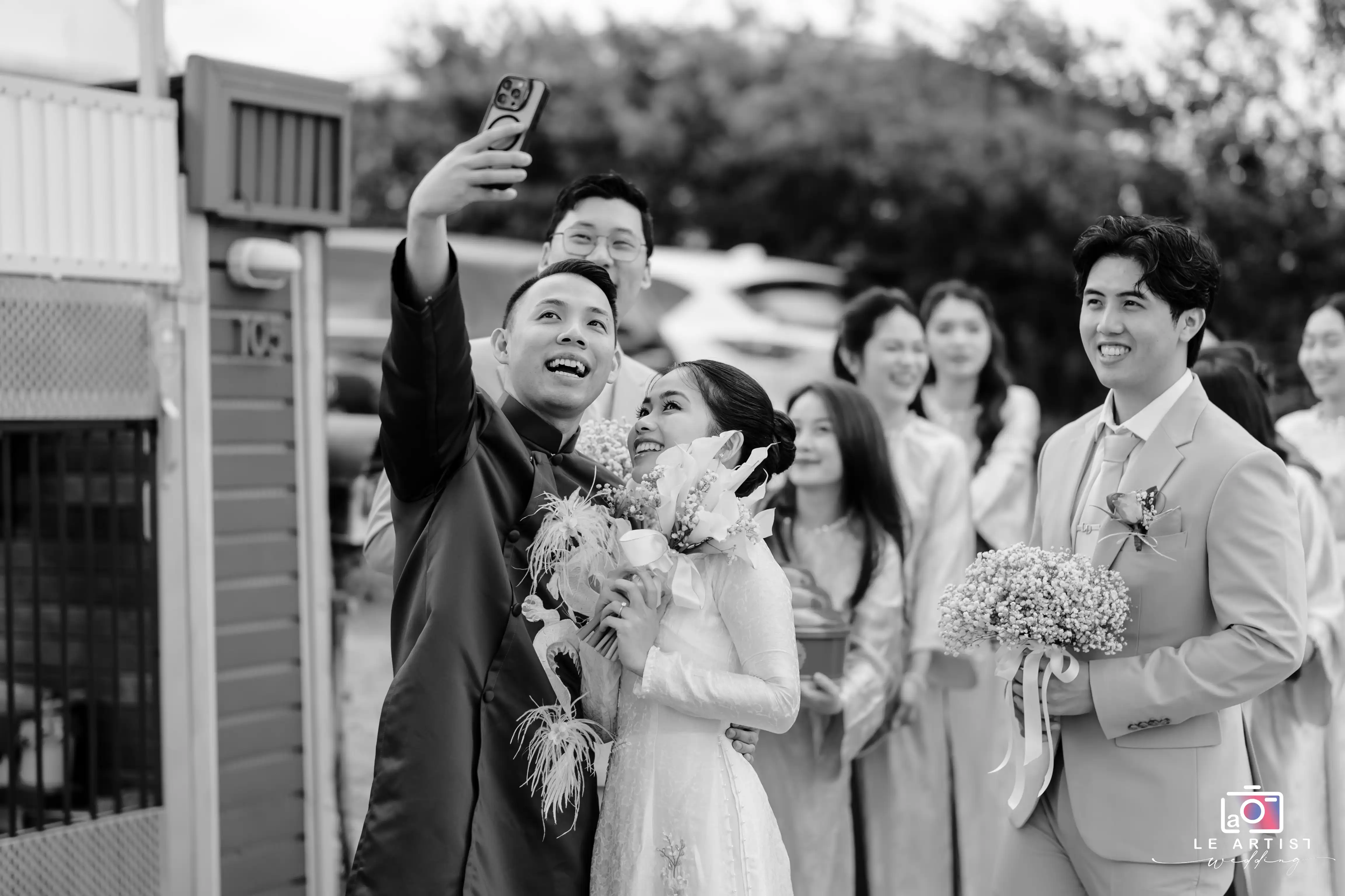 A joyful moment captured as the bride and groom take a cheerful selfie with their friends, celebrating their special day together. Le Artist Wedding