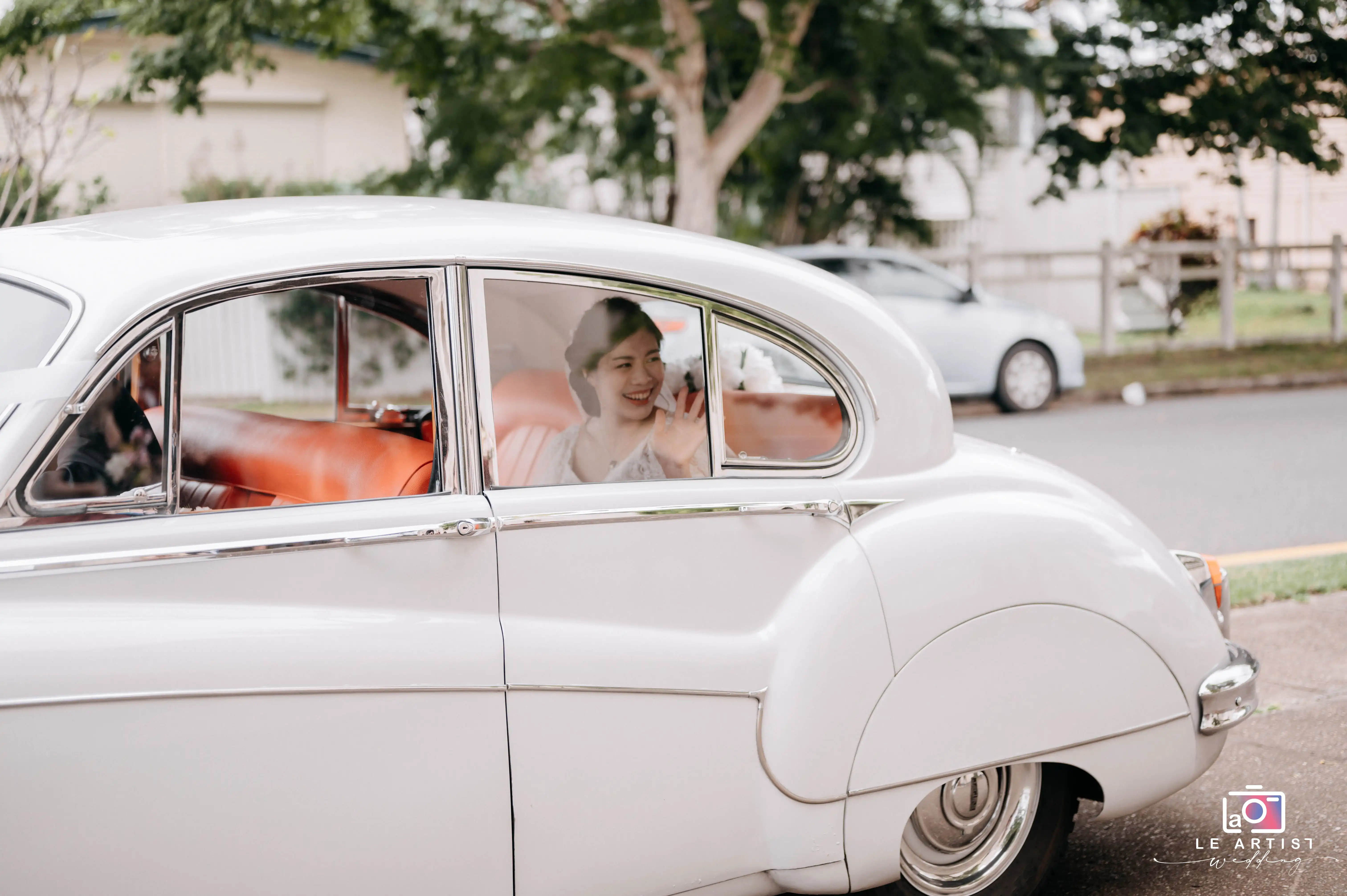 The bride smiles and waves from the car, capturing a beautiful moment before the ceremony. Le Artist Wedding