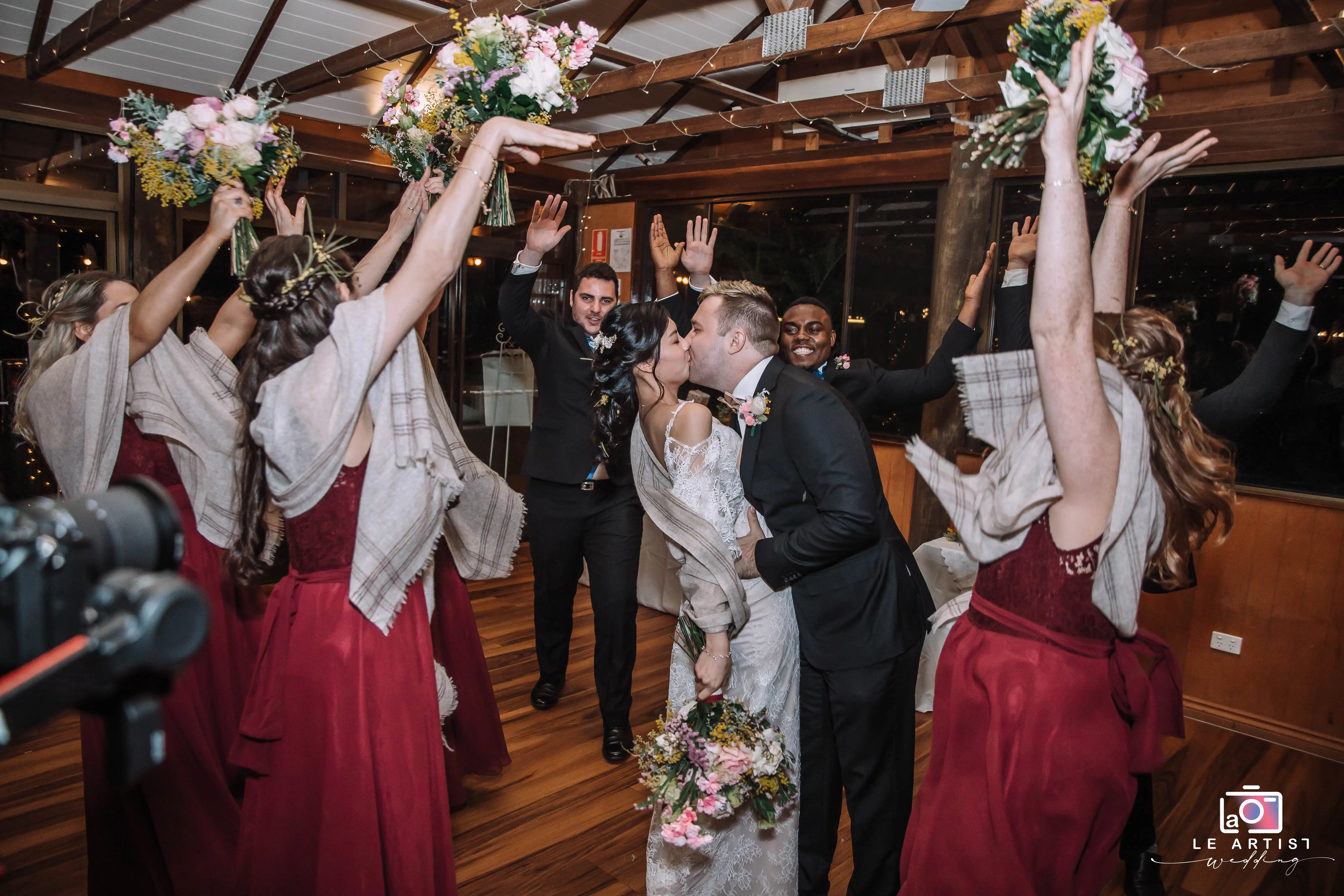 The newlyweds share a joyful kiss surrounded by their cheering bridal party. Le Artist Wedding
