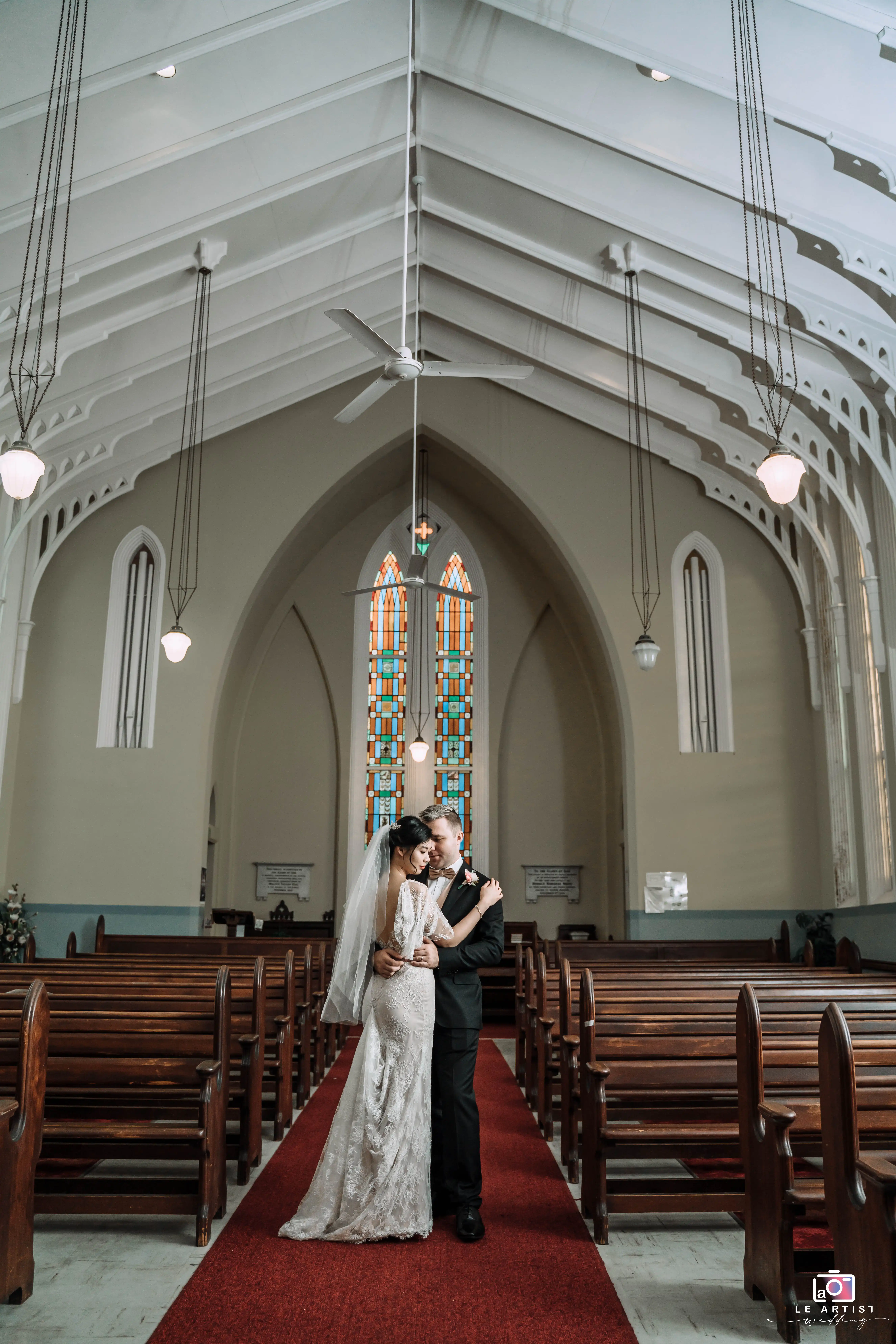 The couple shares an intimate moment under the beautiful architecture of the church, standing together on the red carpet in the aisle. Le Artist Wedding