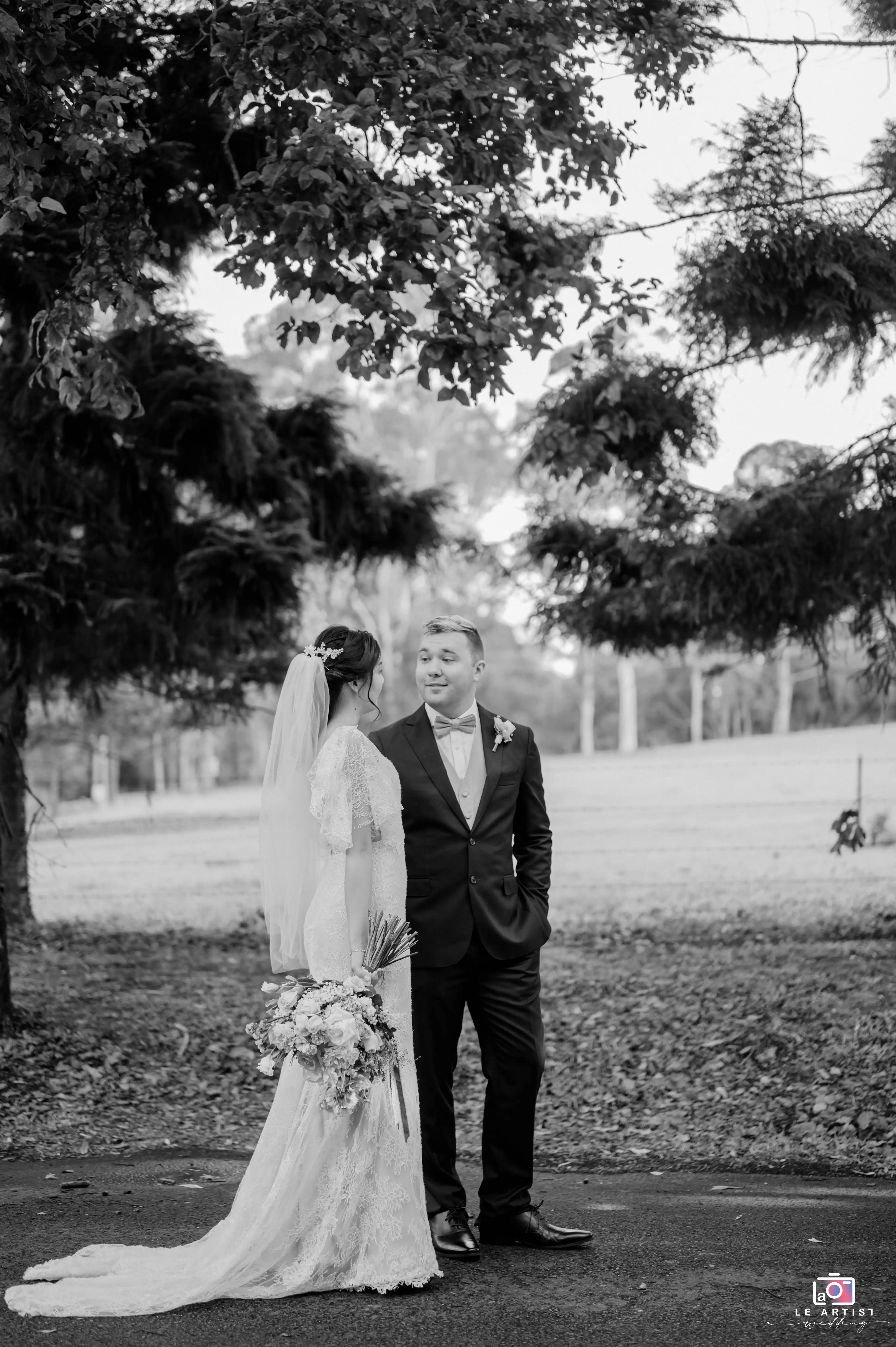 A romantic black-and-white portrait of the bride and groom sharing a moment surrounded by lush greenery. Le Artist Wedding
