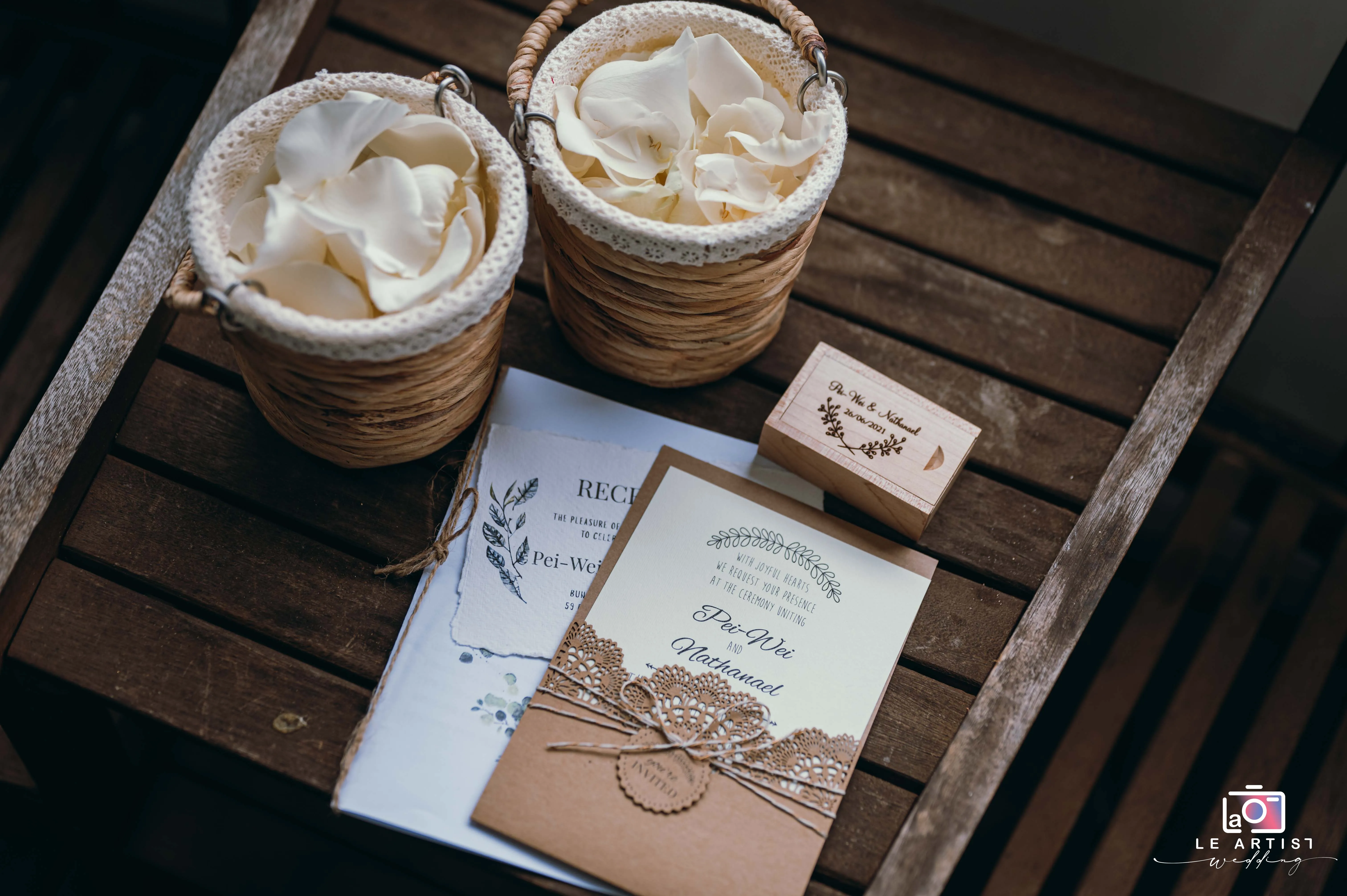 Elegant wedding stationery with rustic baskets of petals on a wooden table, showcasing personalized details for Pei-Wei and Nathanael's special day. Le Artist Wedding