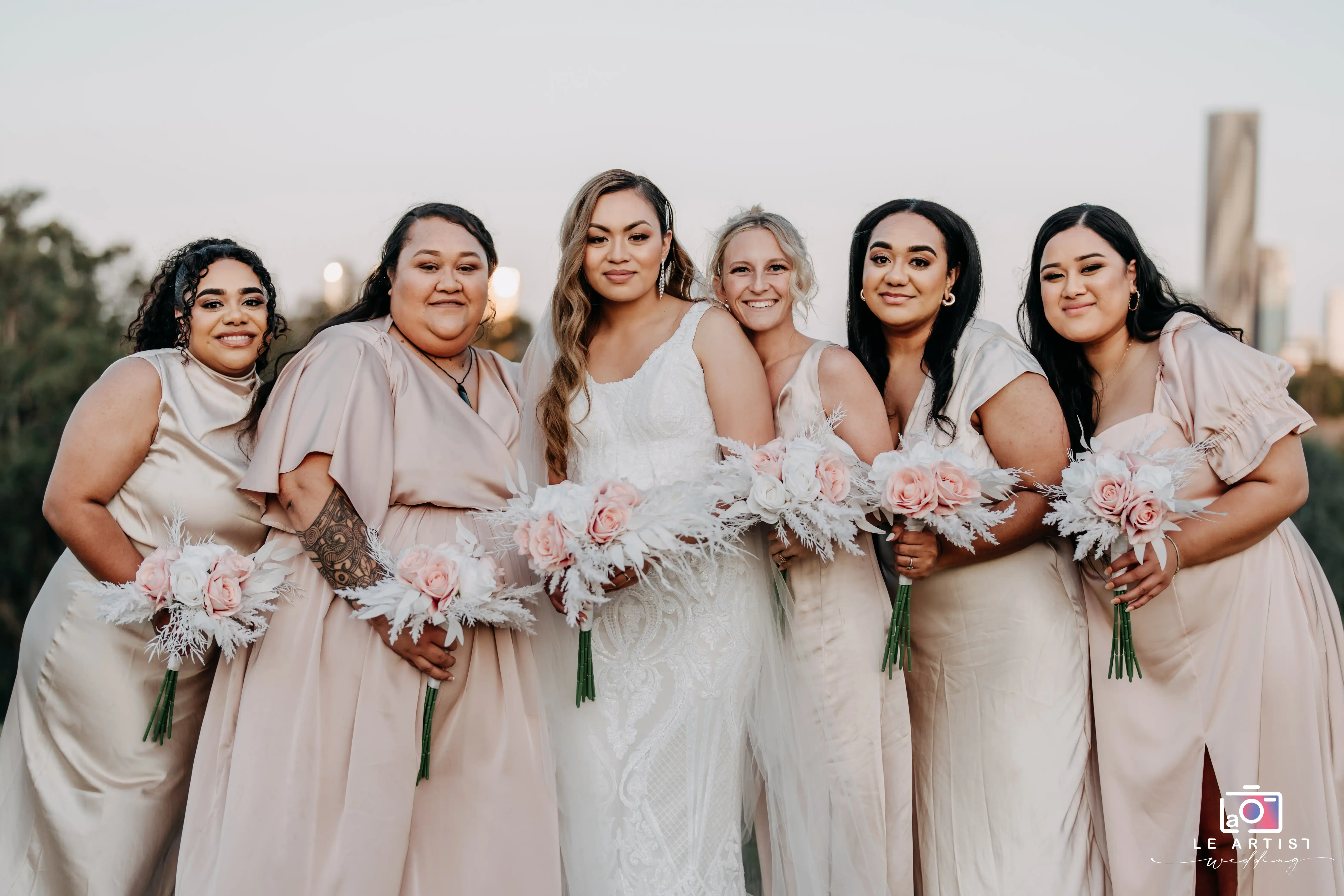 The bride poses with her bridal party, each holding a delicate bouquet of pink and white flowers. Le Artist Wedding