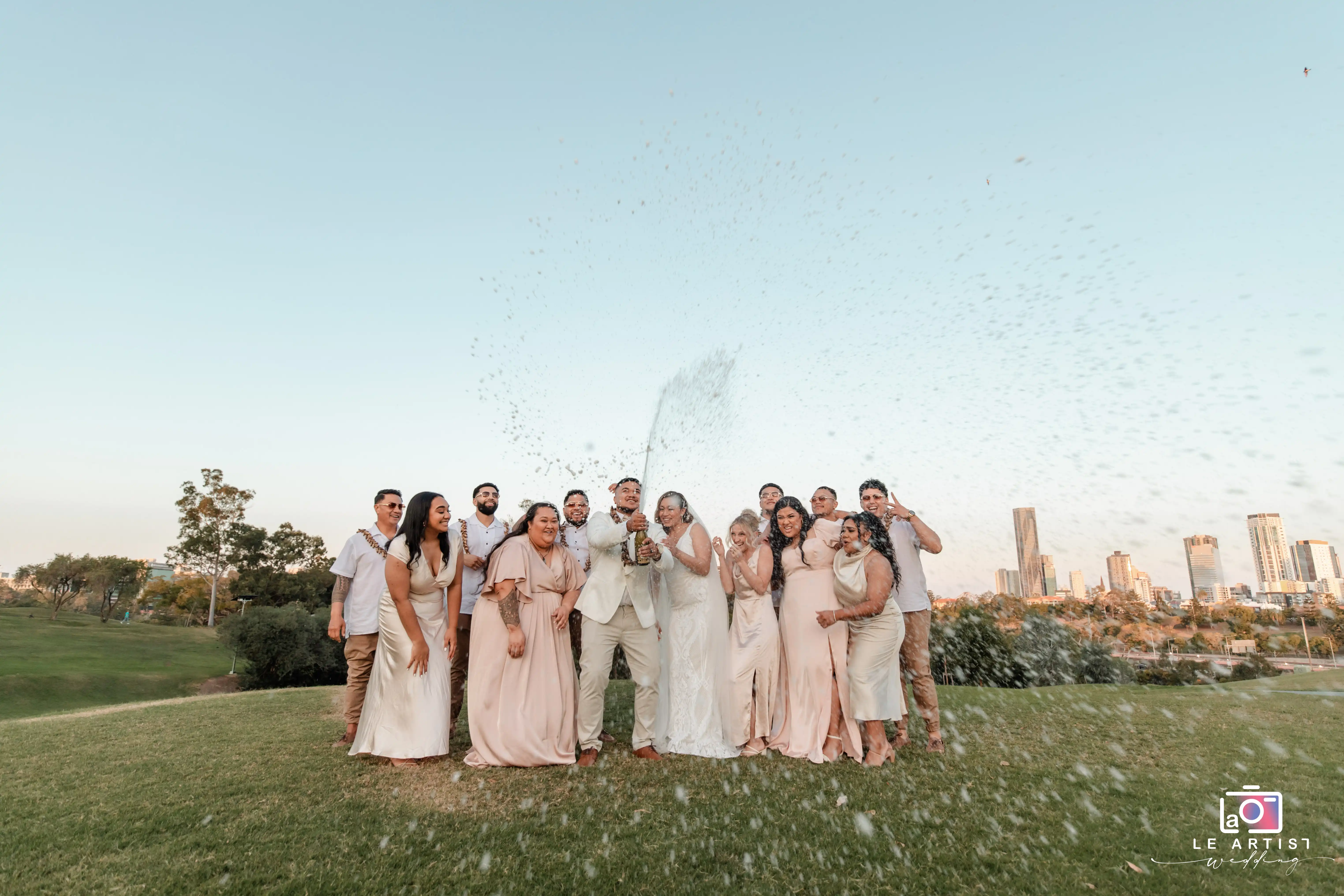 The joyous bridal party celebrates with a champagne spray against a scenic city backdrop. Le Artist Wedding