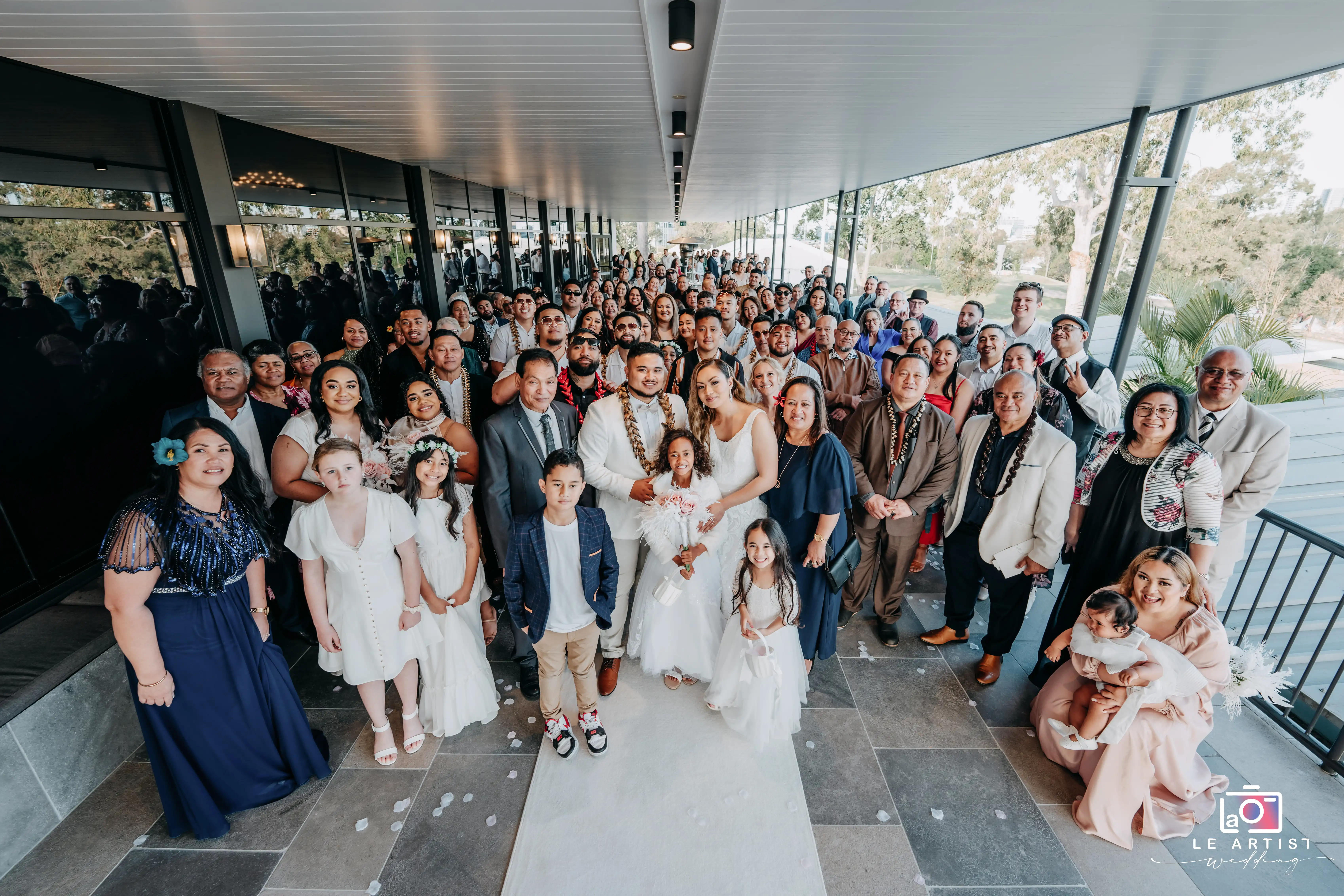 A joyful and inclusive group photo with the newlyweds and their guests, capturing the essence of celebration and family during the wedding day. Le Artist Wedding