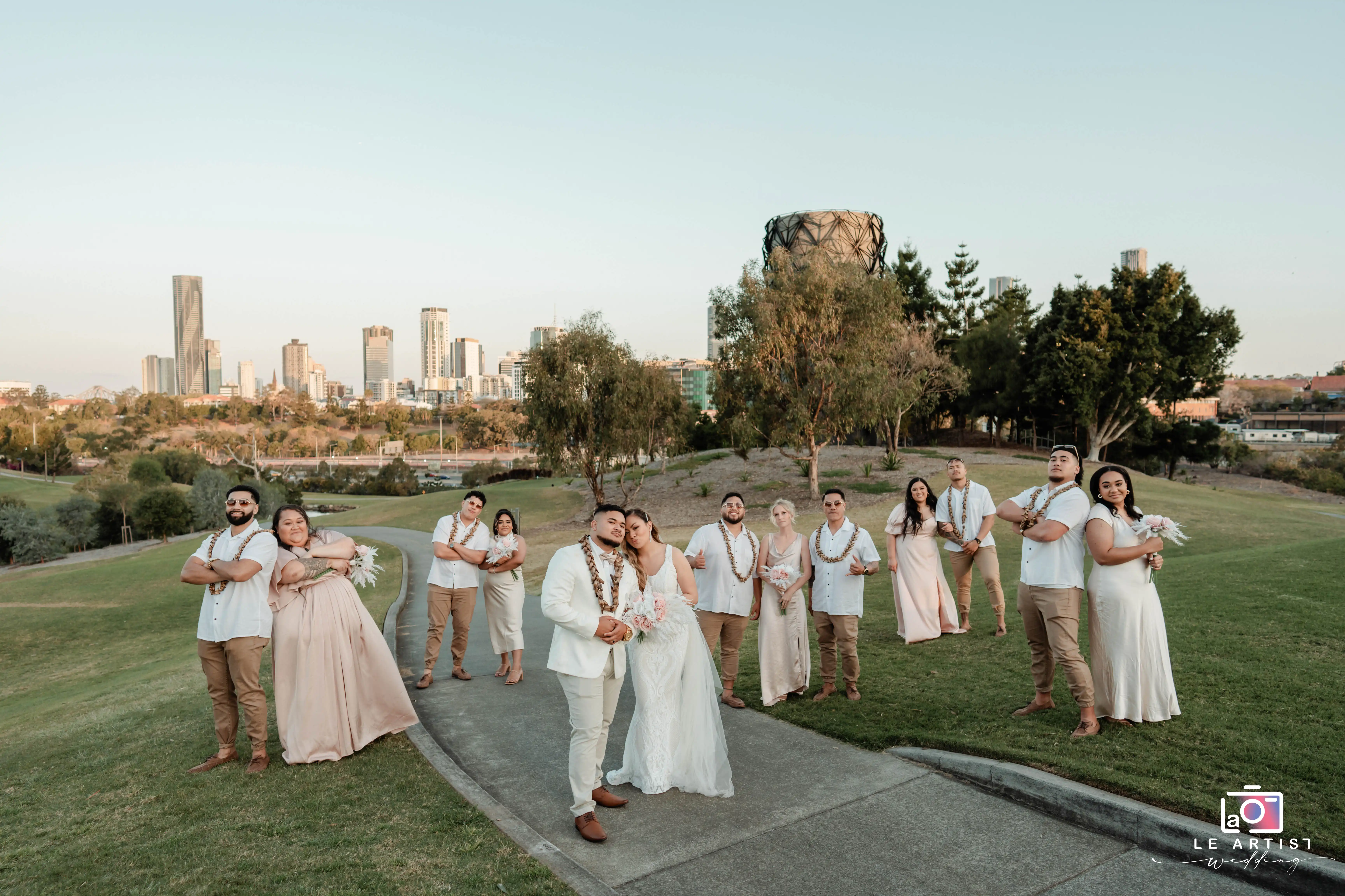The couple shares a joyful moment with their bridal party against a scenic city backdrop. Le Artist Wedding
