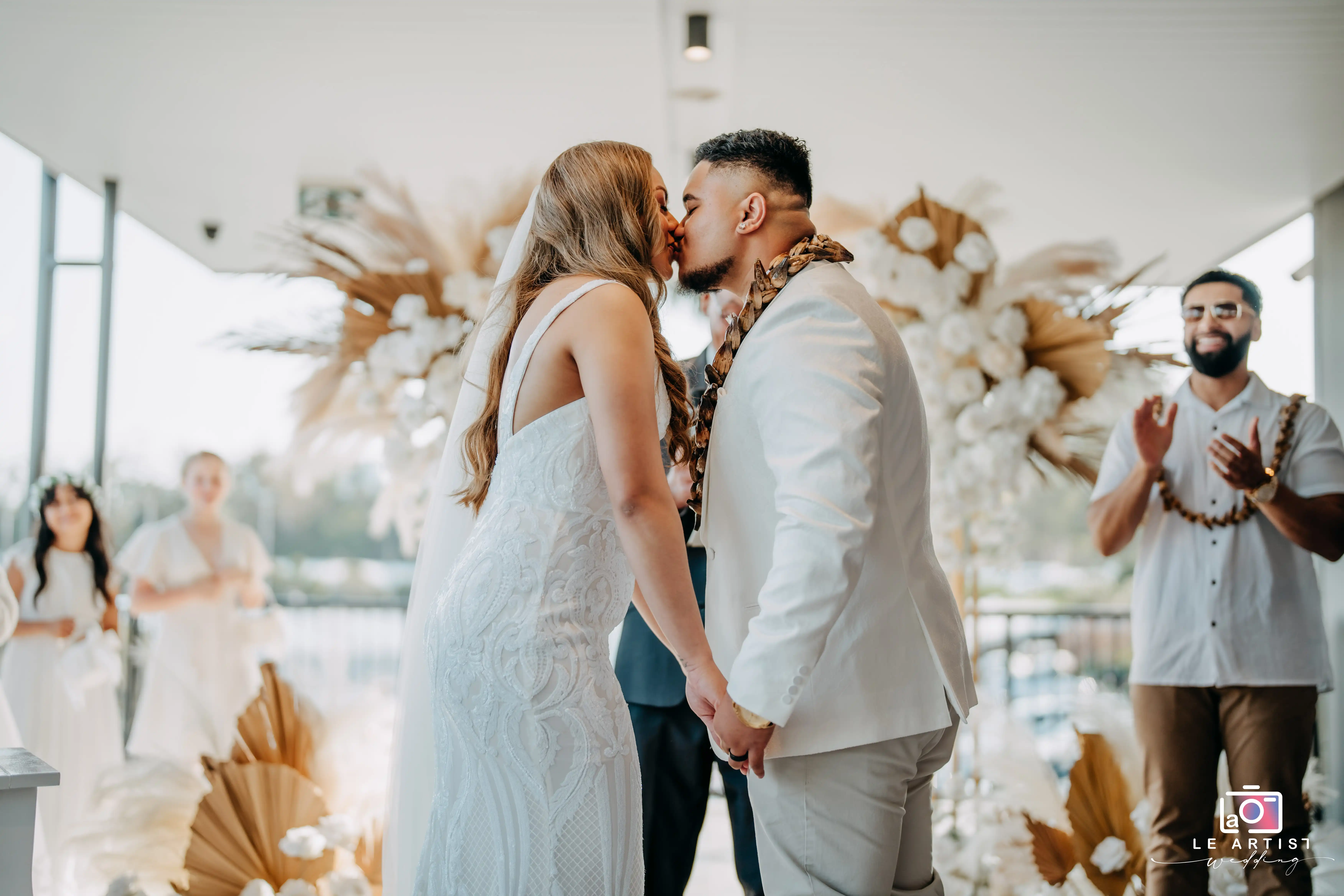 The couple shares a kiss during the ceremony as onlookers clap in celebration. Le Artist Wedding