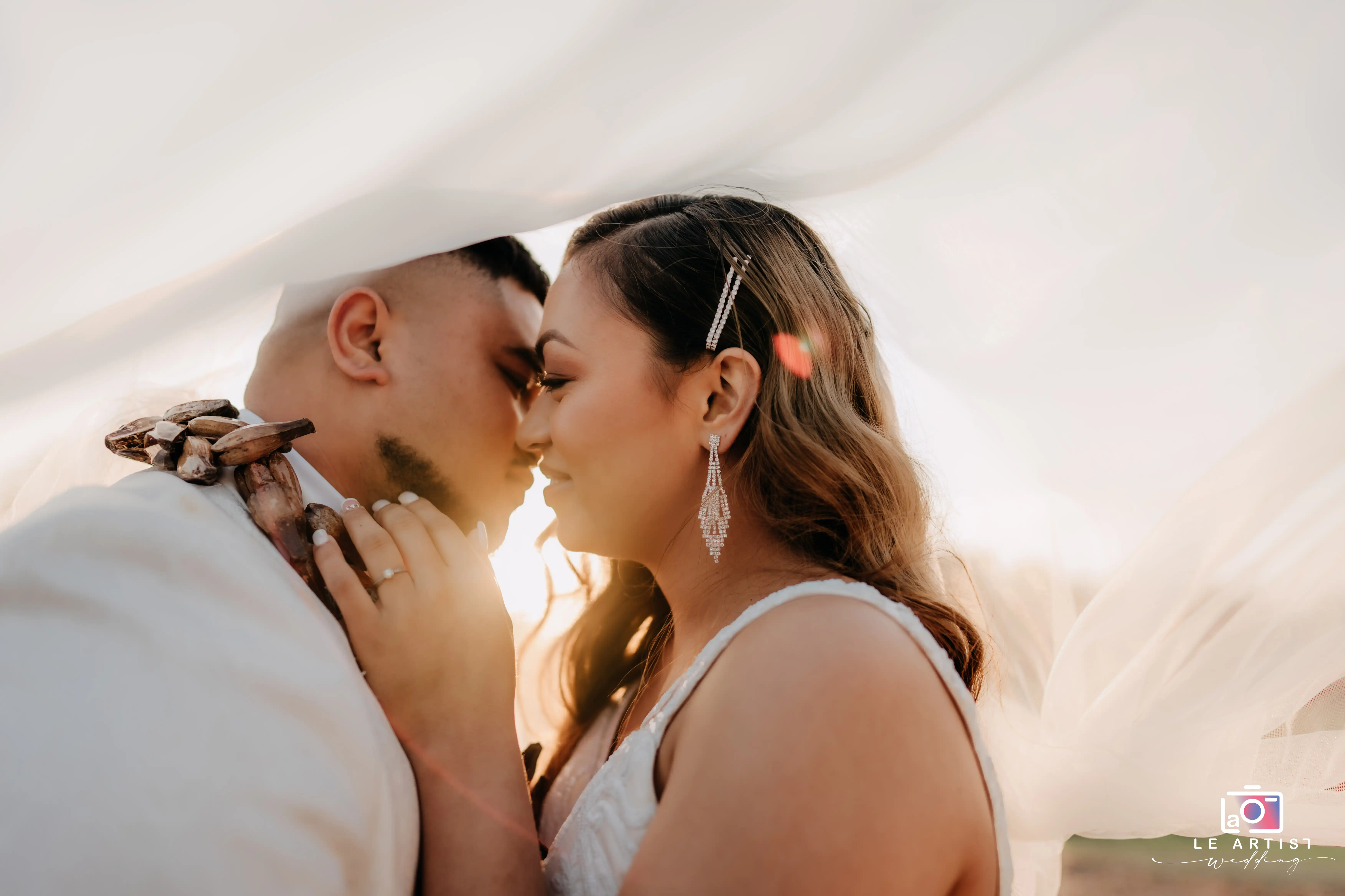 A tender moment as the couple shares a kiss under the veil, capturing their intimacy and love. Le Artist Wedding