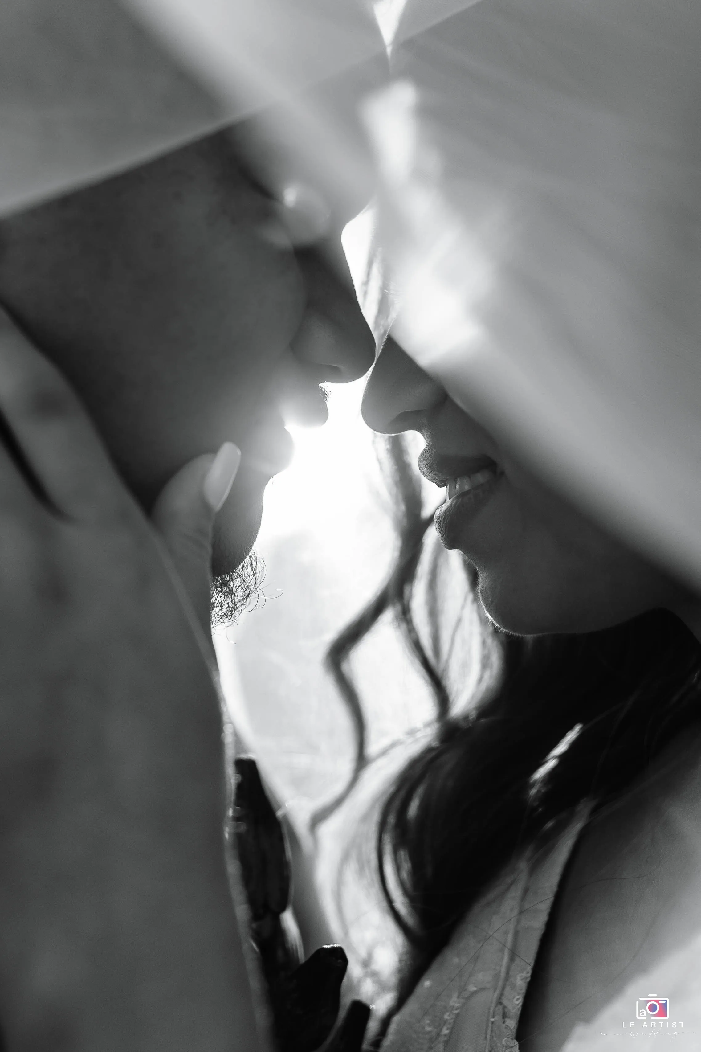 A tender moment of the couple sharing a kiss, captured beneath the veil in soft black and white. Le Artist Wedding