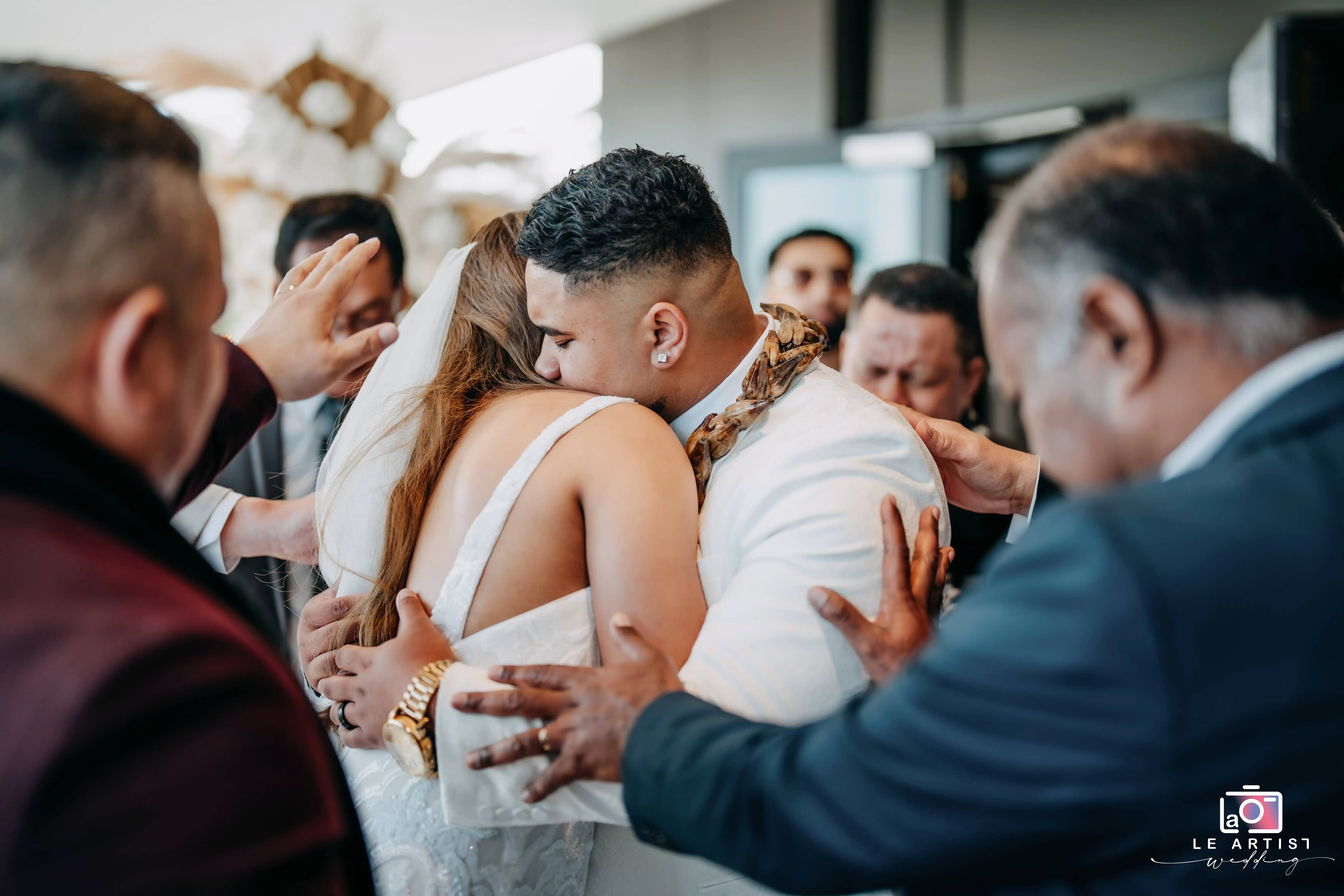 The couple share an emotional embrace during the ceremony processional, surrounded by the supportive hands of loved ones. Le Artist Wedding