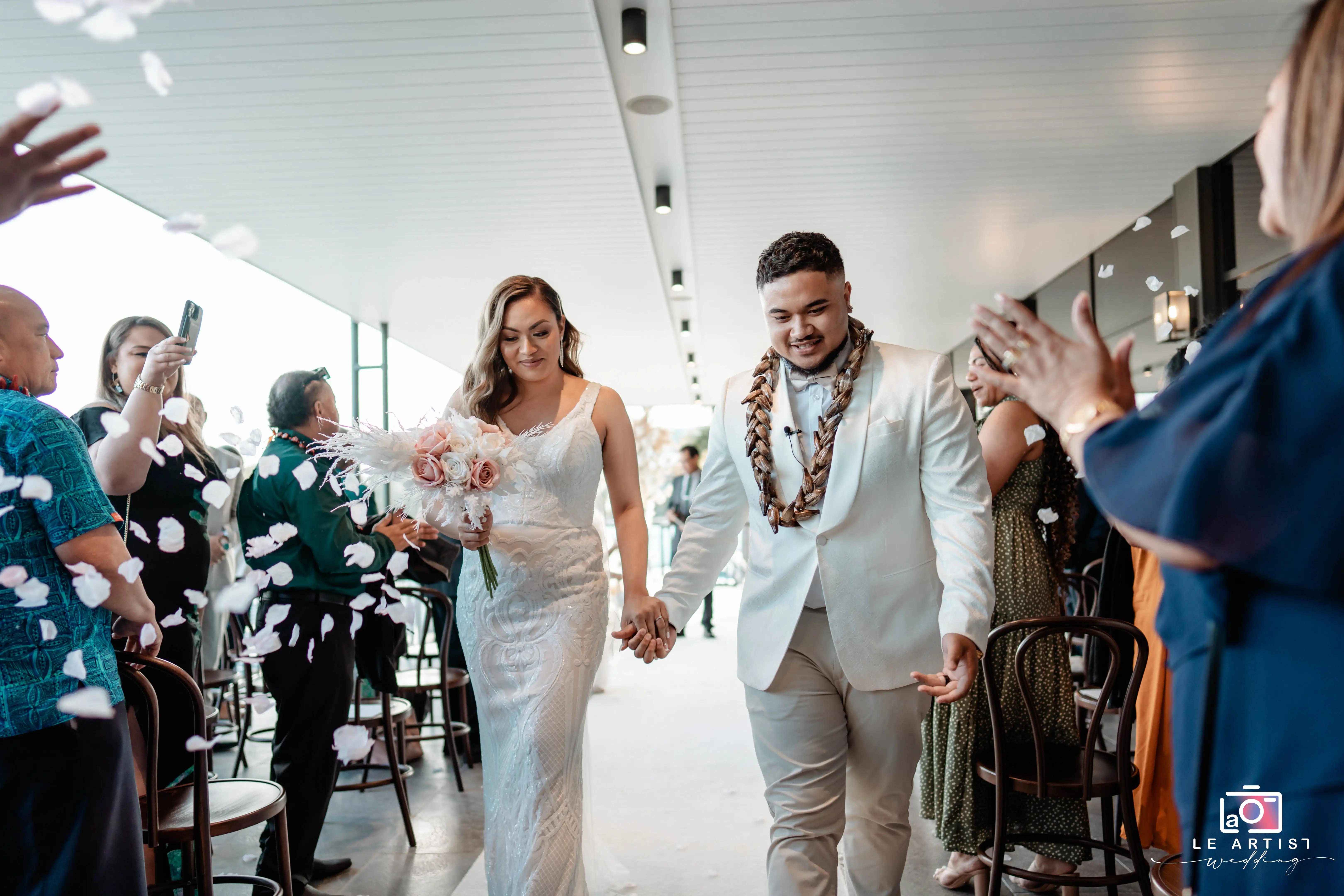 The newlyweds joyfully walk down the aisle as guests shower them with petals, celebrating their union. Le Artist Wedding
