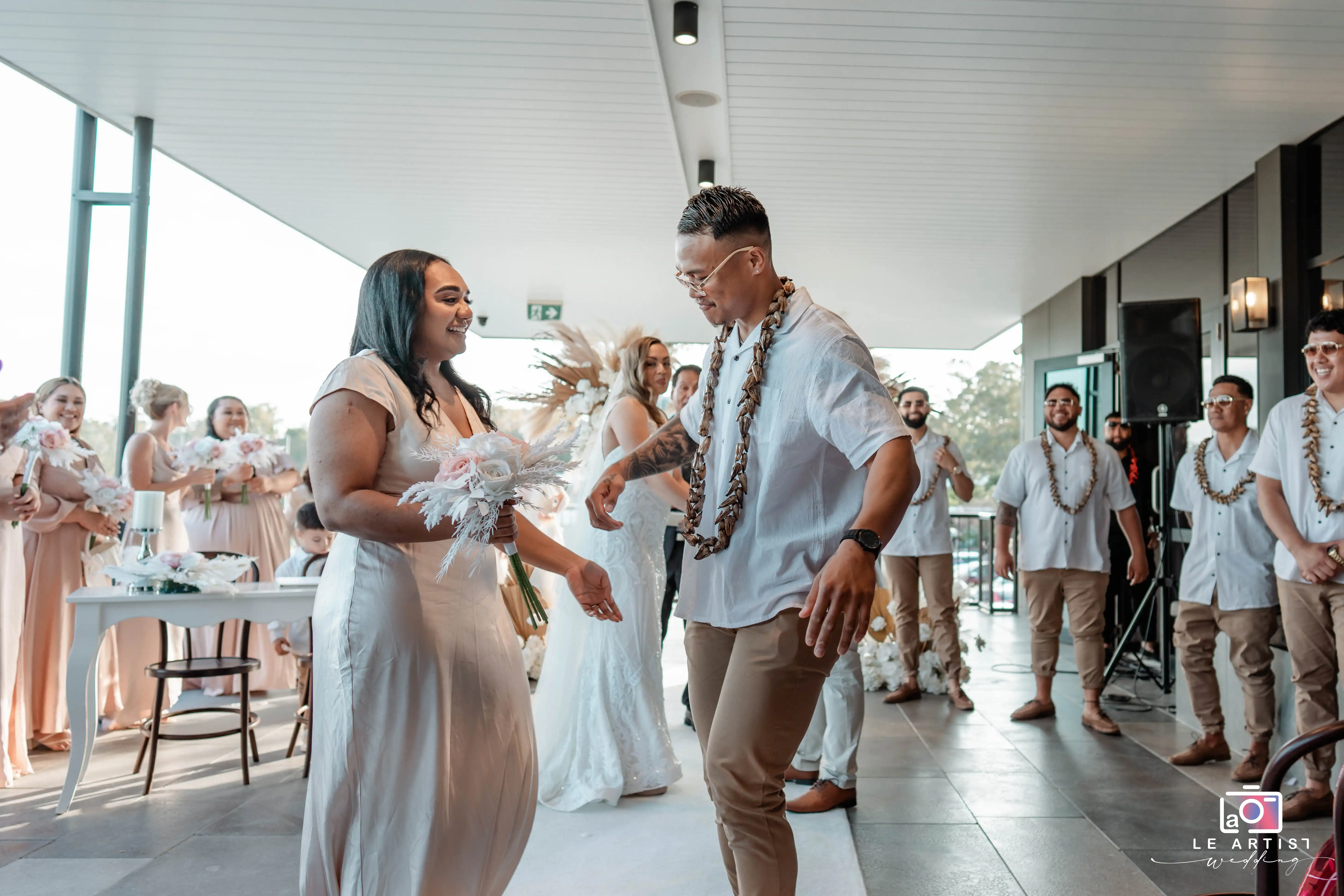 The couple joyfully dances together, surrounded by their bridesmaids and groomsmen during the wedding reception. Le Artist Wedding