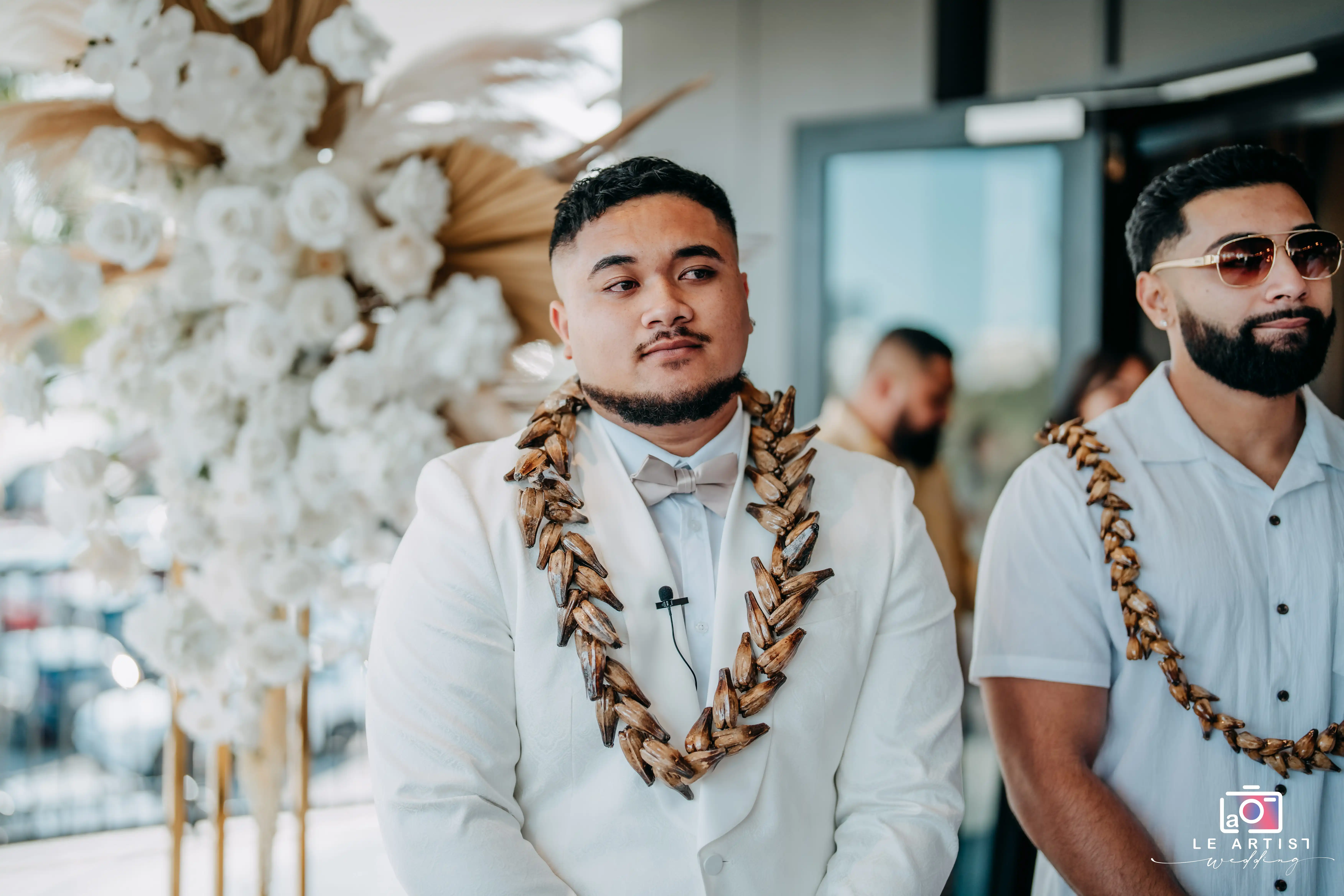 The groom and his groomsman adorned with traditional lei, preparing to walk down the aisle during the ceremony processional. Le Artist Wedding