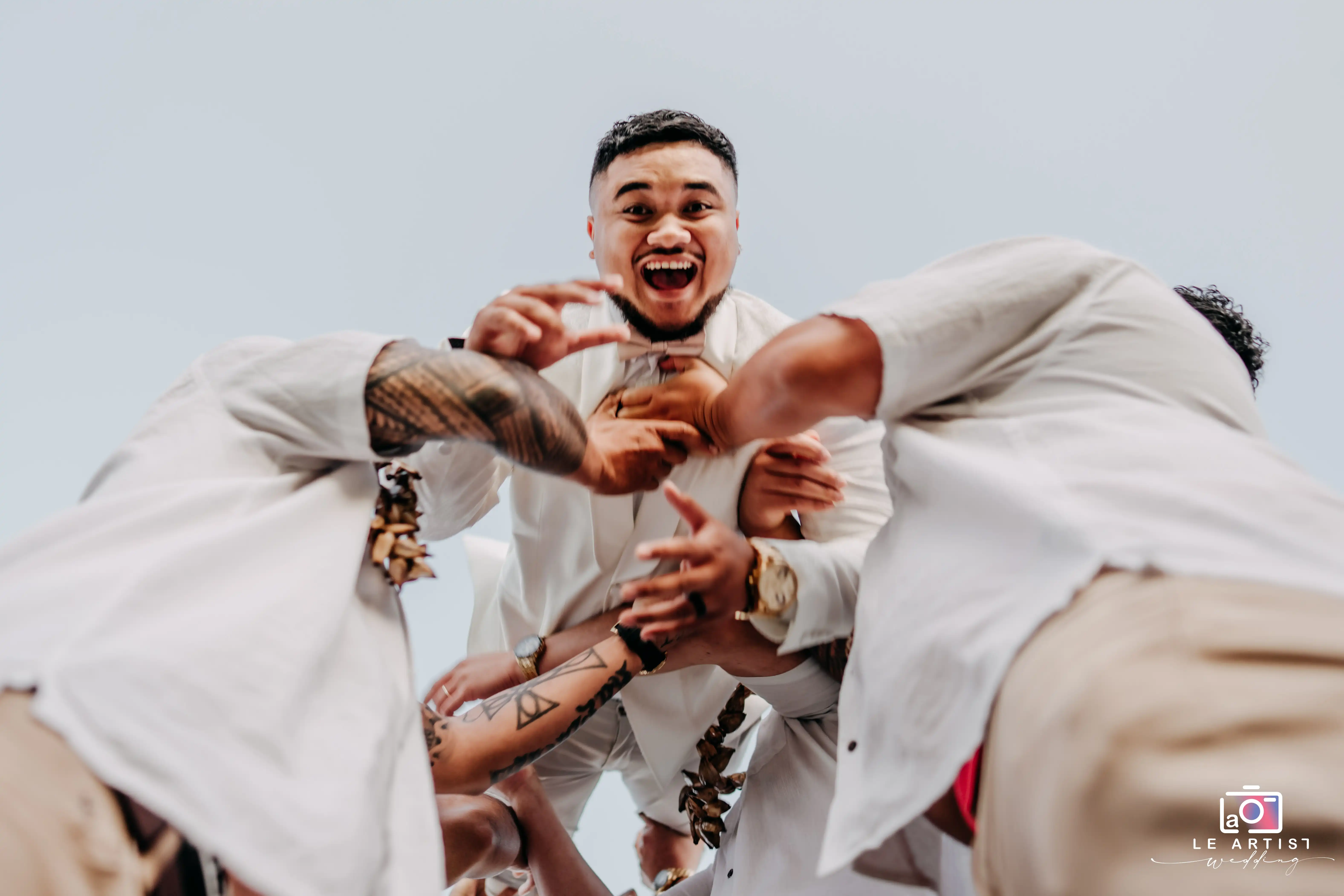 Groom surrounded by groomsmen in a joyful and energetic moment during the bridal party photoshoot. Le Artist Wedding