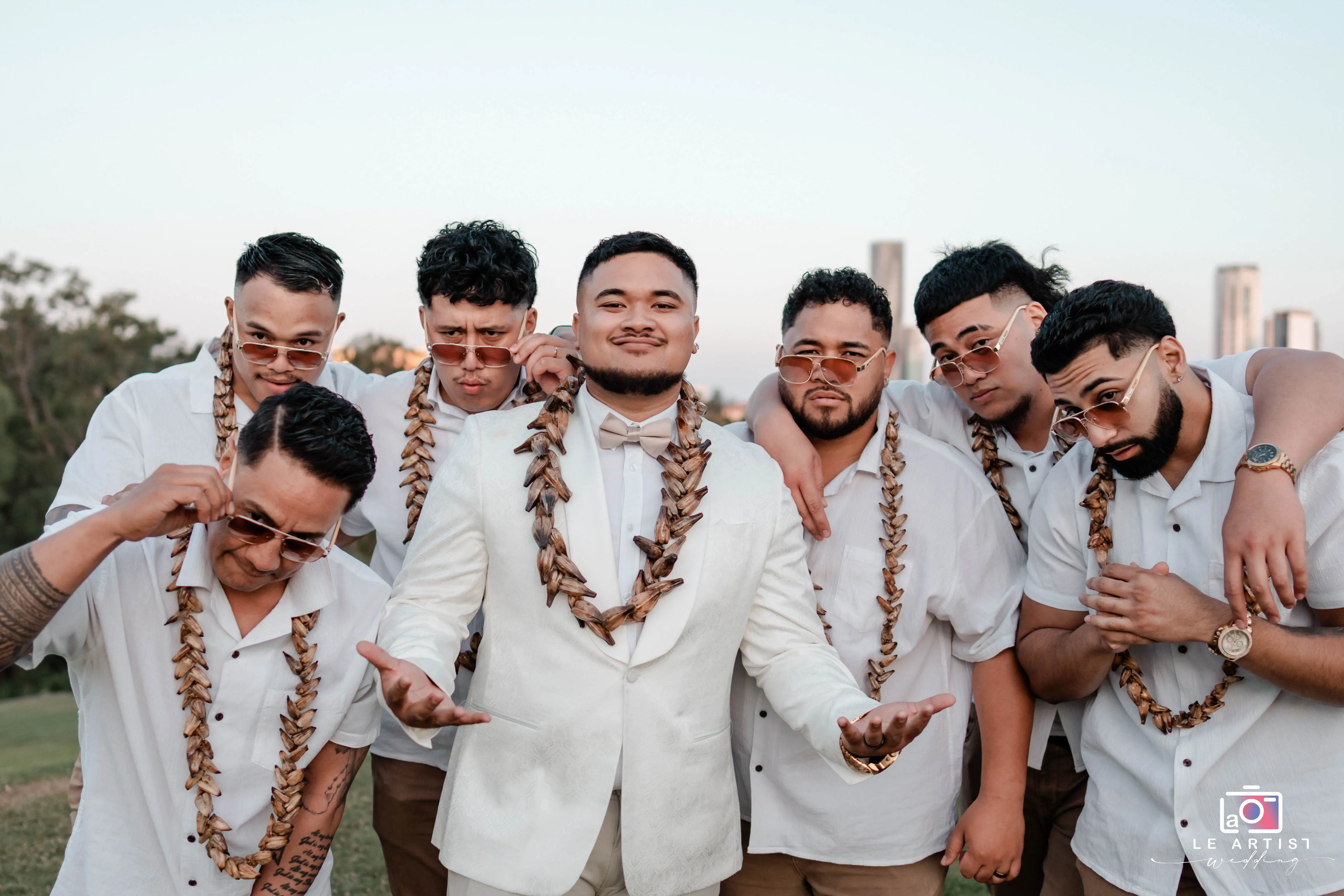 The groom and his groomsmen strike a confident pose, showing off their stylish sunglasses and matching leis. Le Artist Wedding