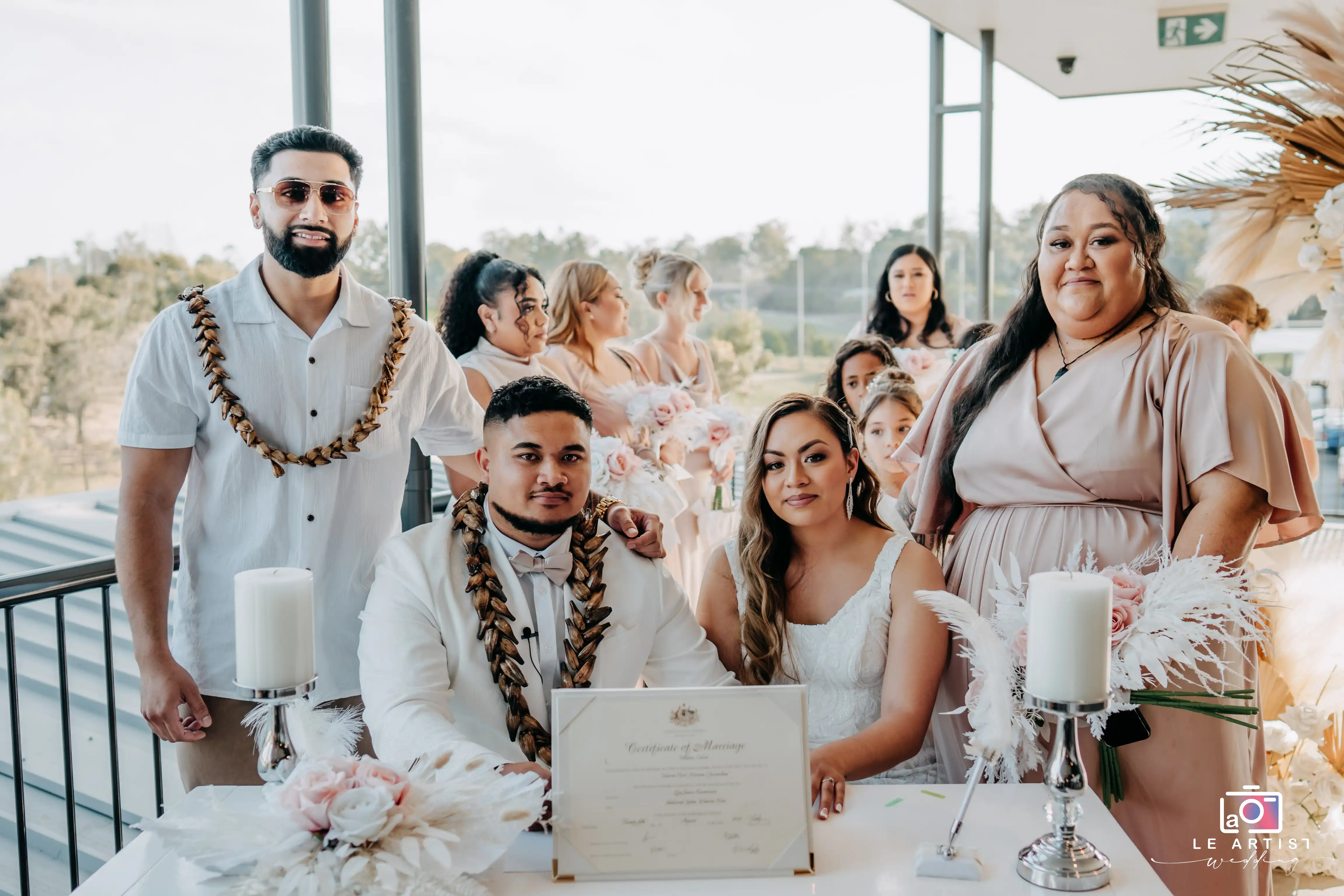 The couple happily poses with their marriage certificate surrounded by friends and family, celebrating their union. Le Artist Wedding