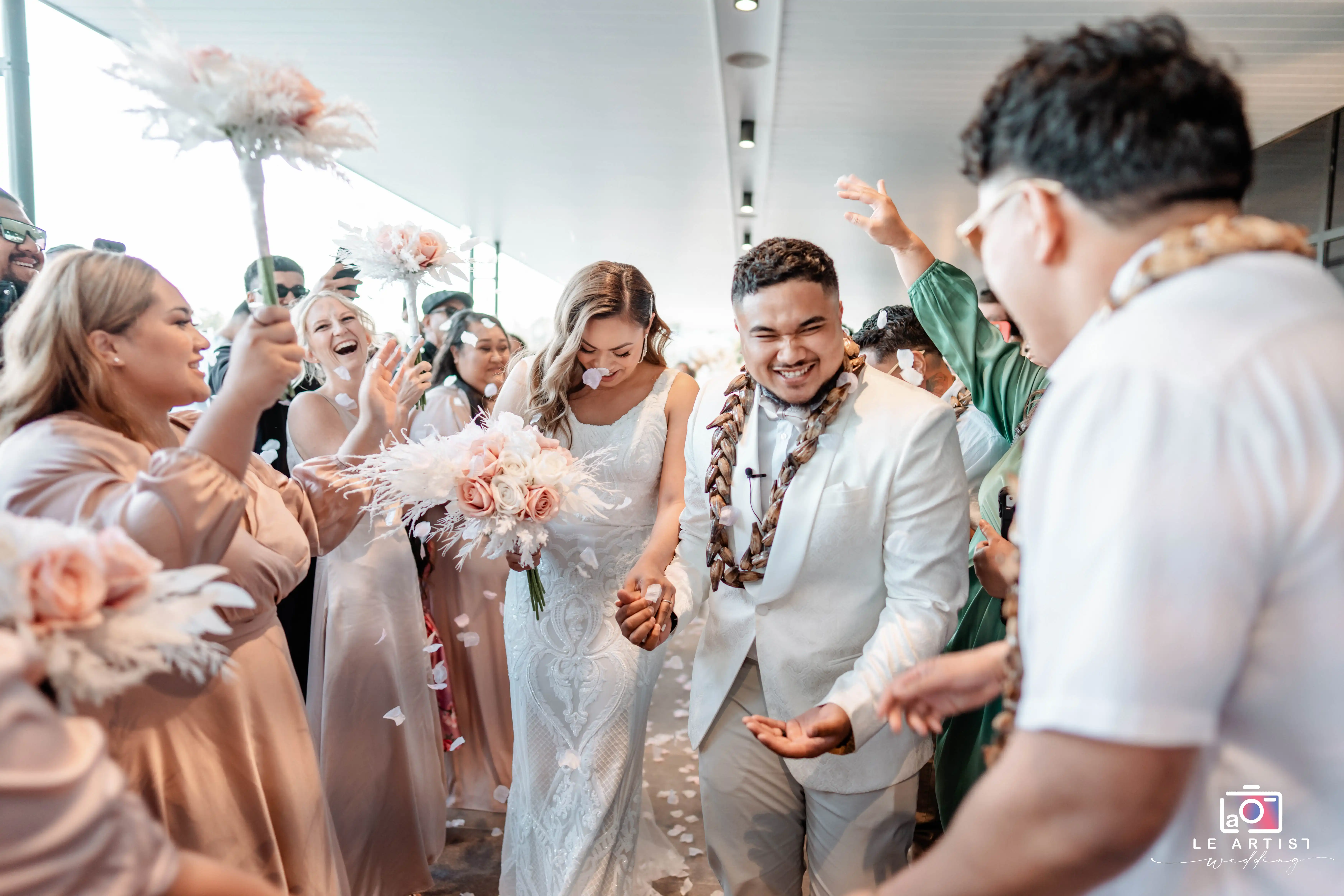 The newlyweds joyfully walk down the aisle as guests celebrate with petals and cheers. Le Artist Wedding