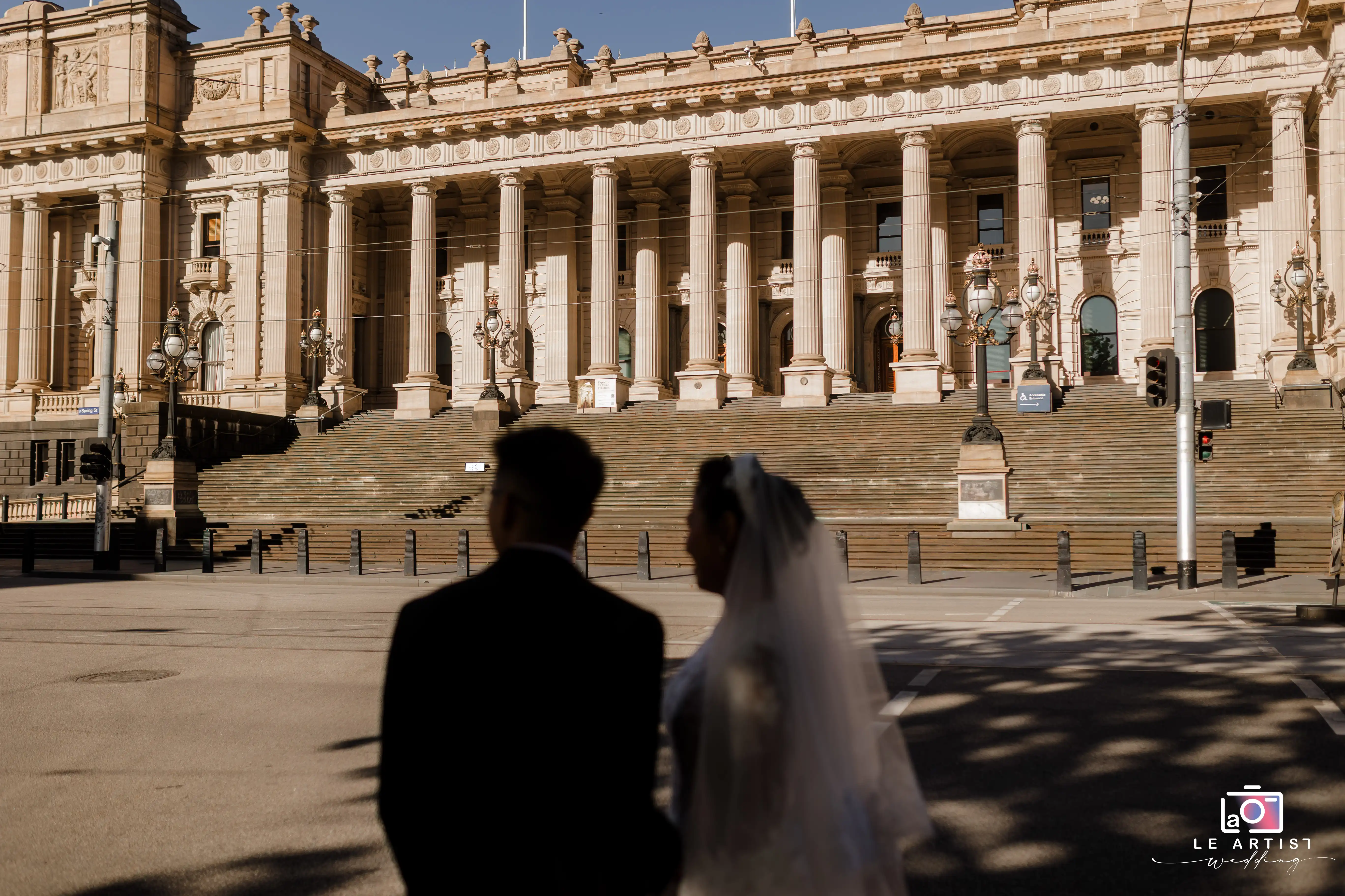 A couple stands together in front of an elegant, historic building, casting silhouettes against the ornate architecture. Le Artist Wedding
