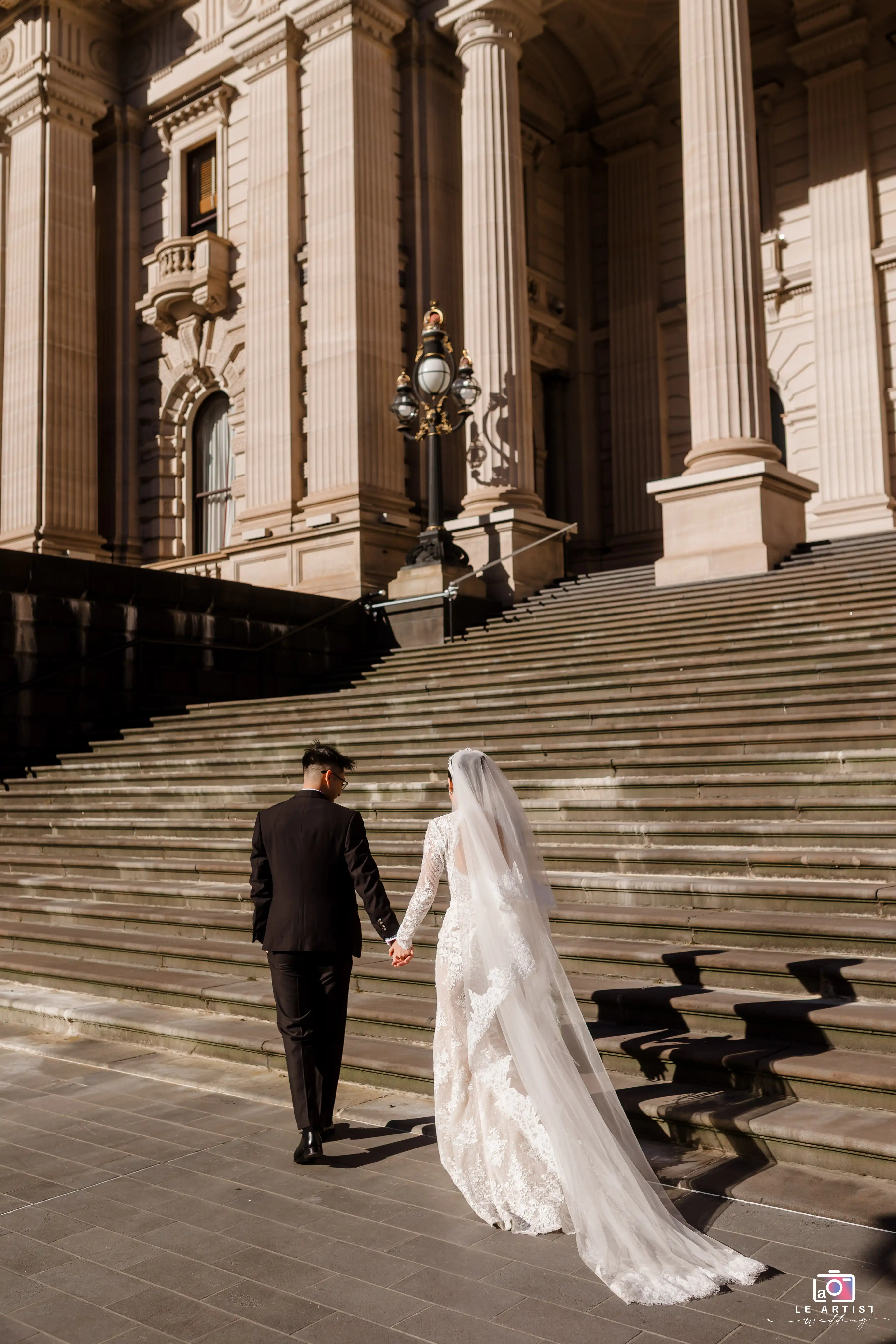 A newlywed couple walks hand in hand up the grand steps of a historic building, beautifully capturing their romantic journey together. Le Artist Wedding