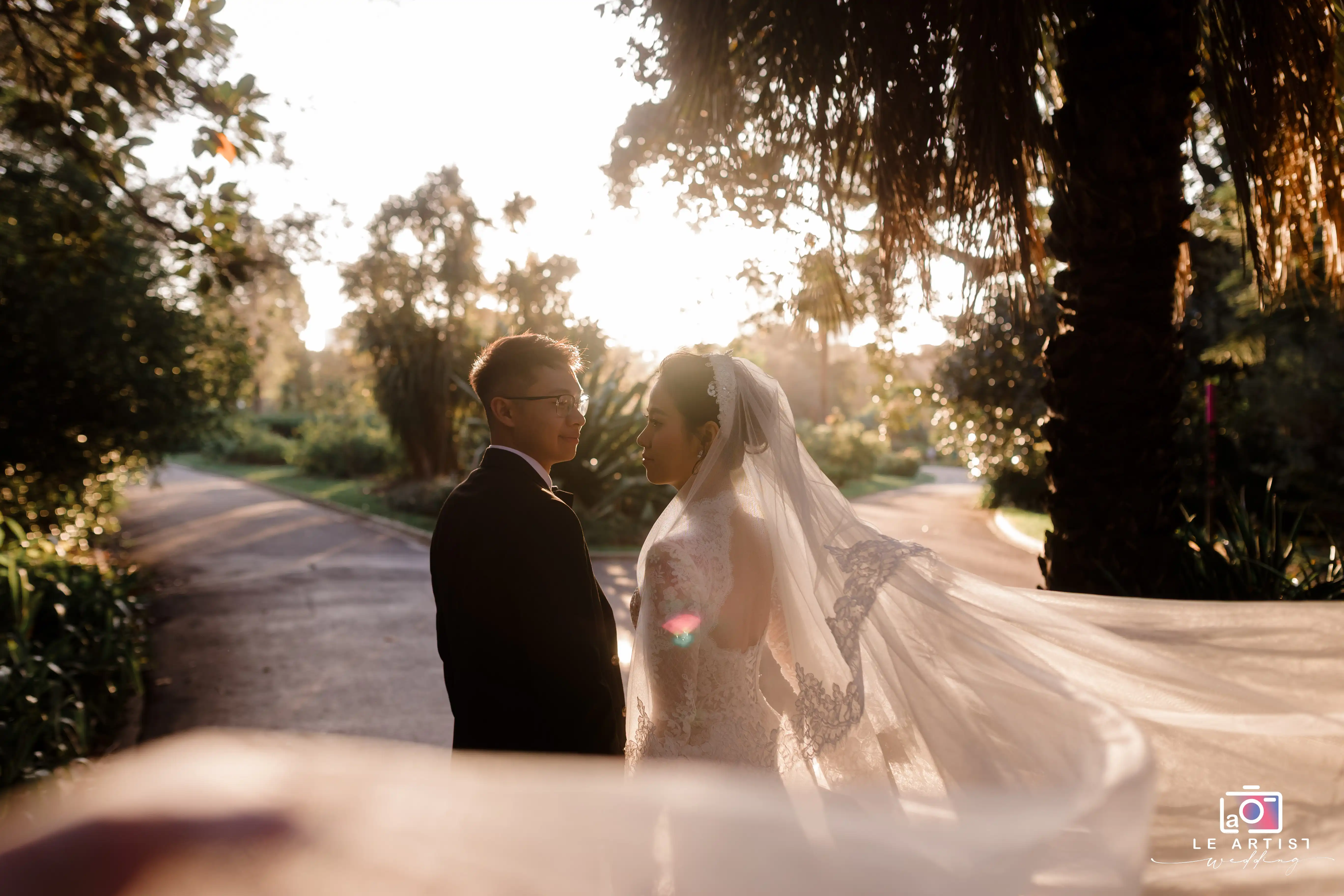 A couple shares an intimate moment in the soft glow of sunset, with the bride's veil gently flowing in the breeze. Le Artist Wedding