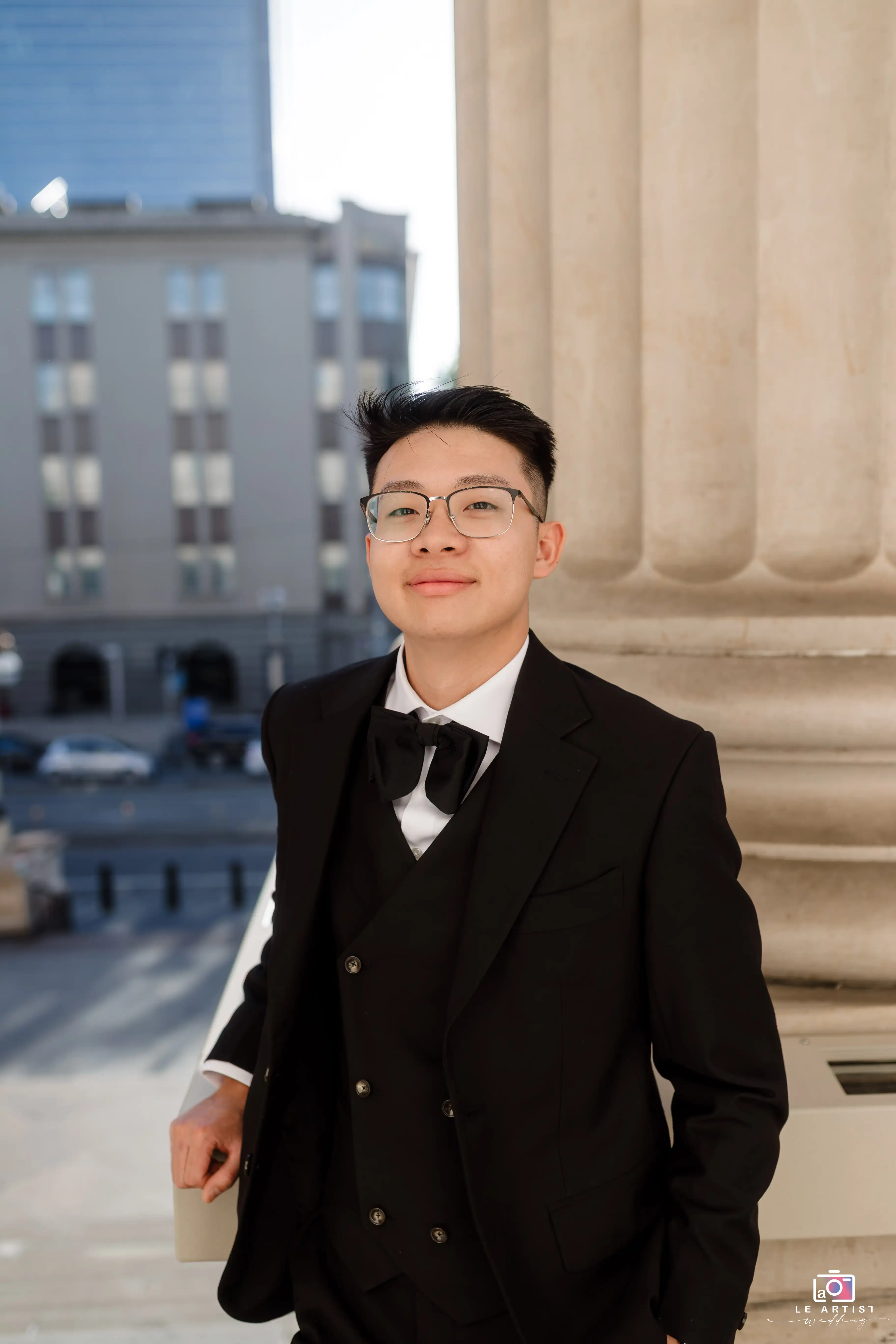 A groom posing confidently in an elegant black suit with an urban backdrop. Le Artist Wedding