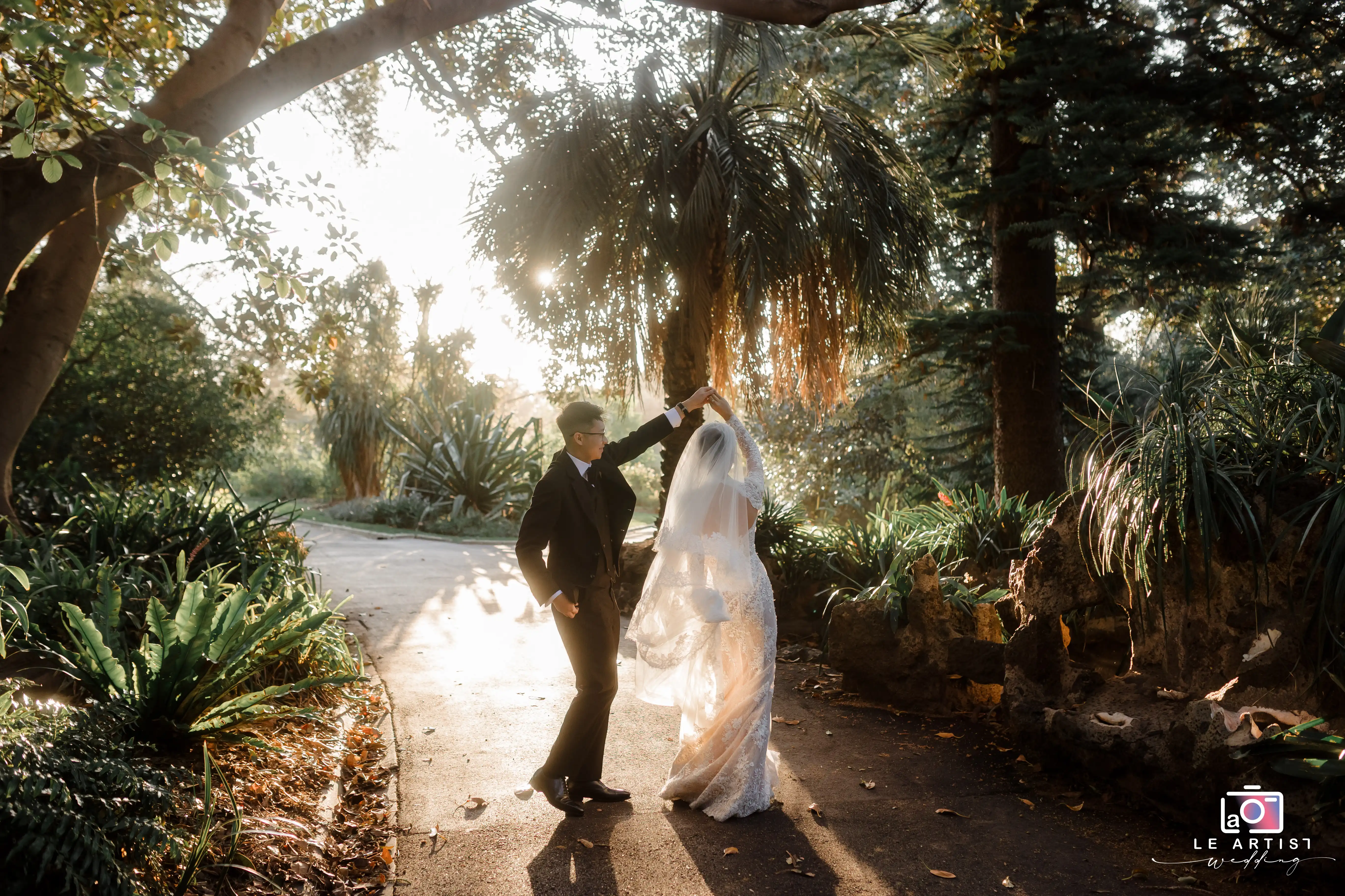 A romantic moment captured as the newlyweds dance gracefully under the golden sunlight in a lush garden setting. Le Artist Wedding